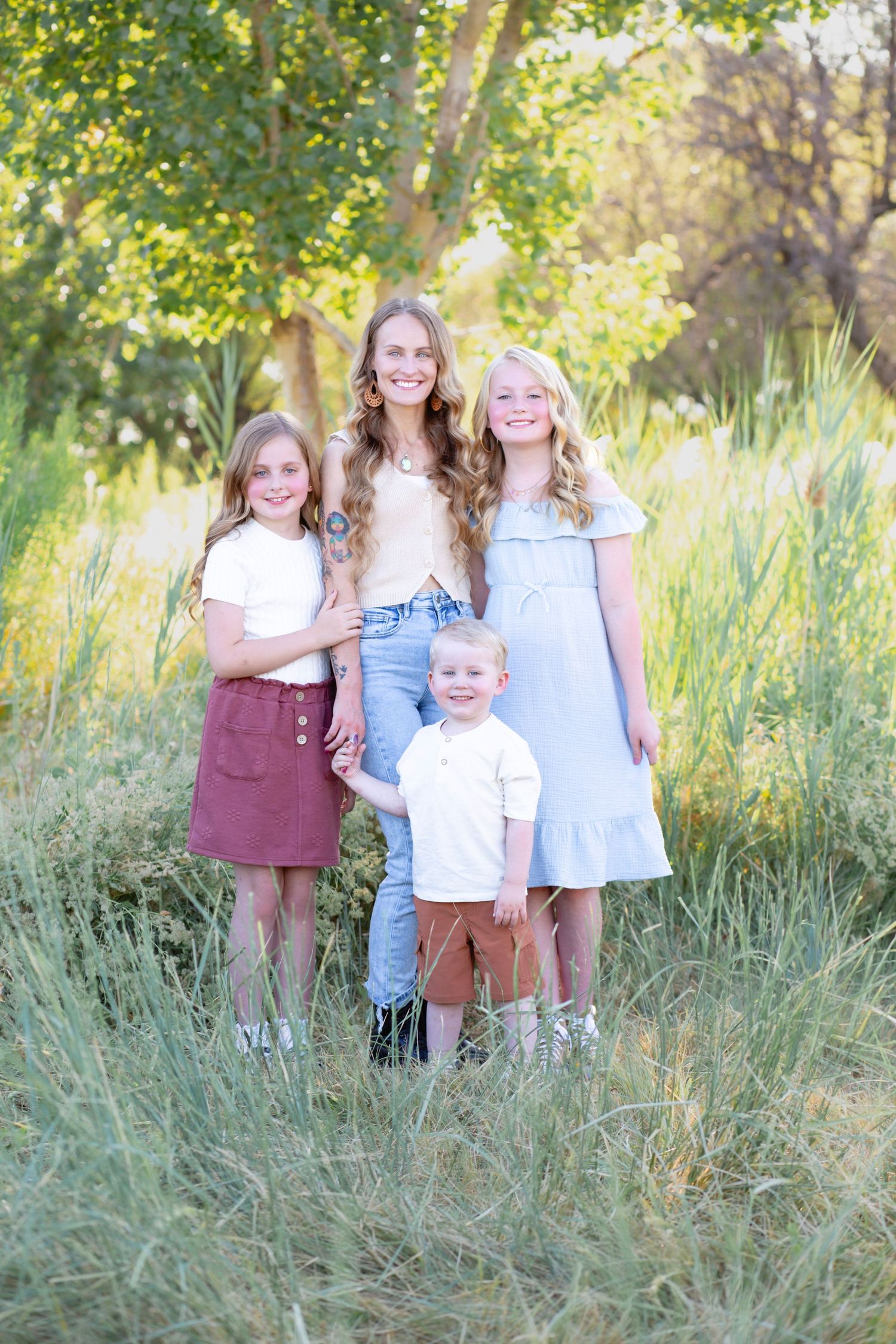 A group of siblings standing together in tall grass with sunlit trees in the background.