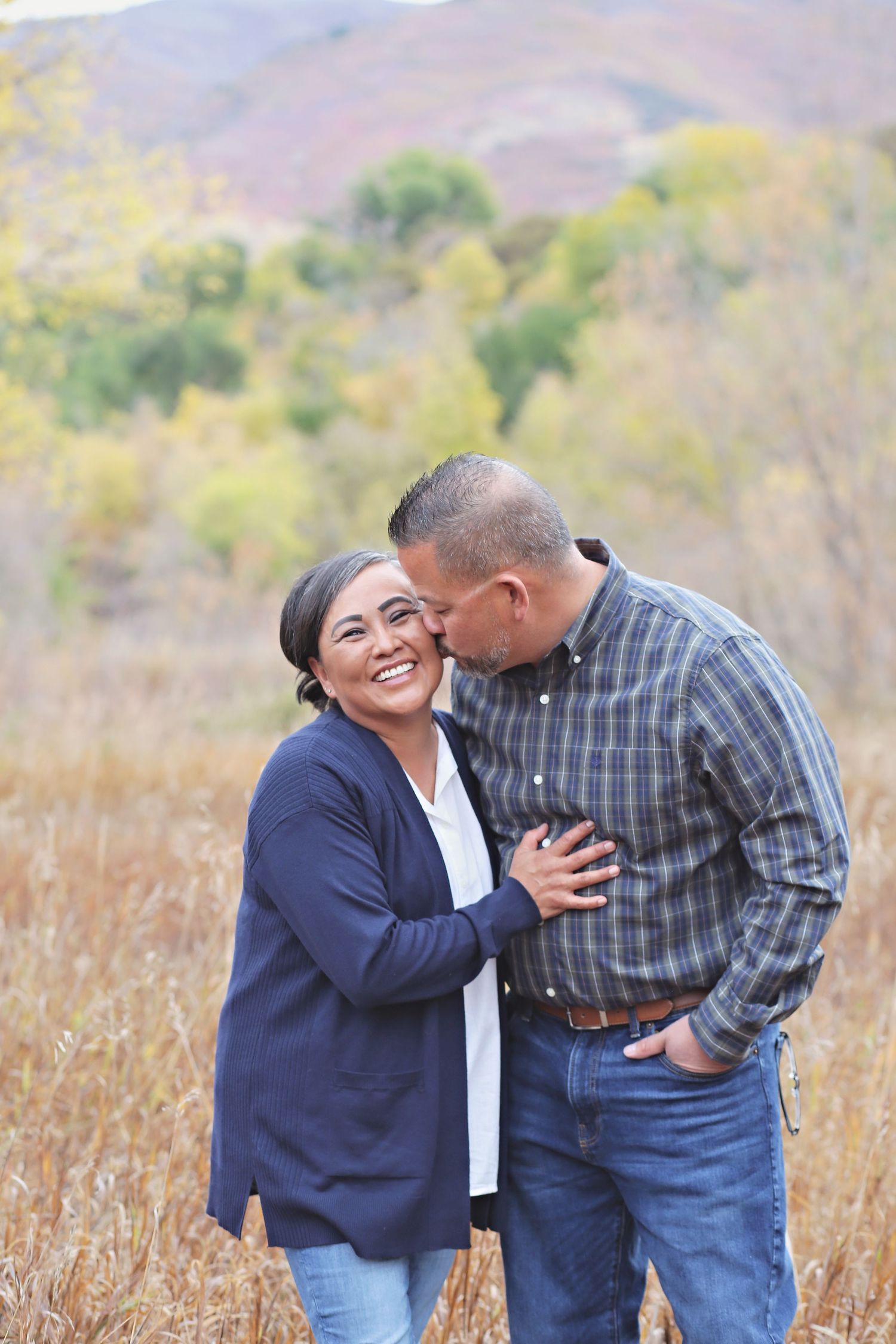 Couple laughing together in a field with mountains in the background during autumn.