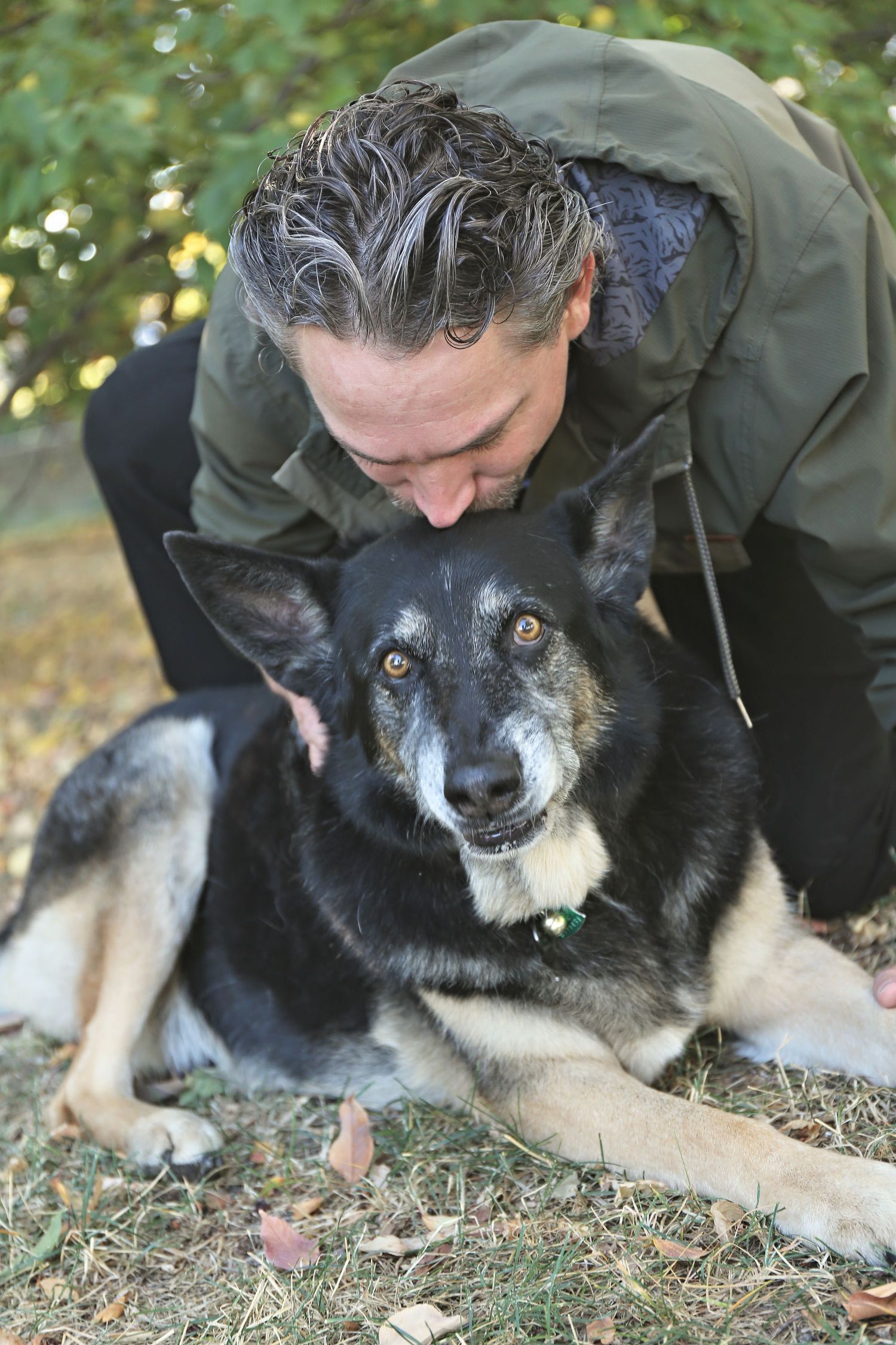 Tender interaction between a dog and someone wearing a green jacket outdoors.