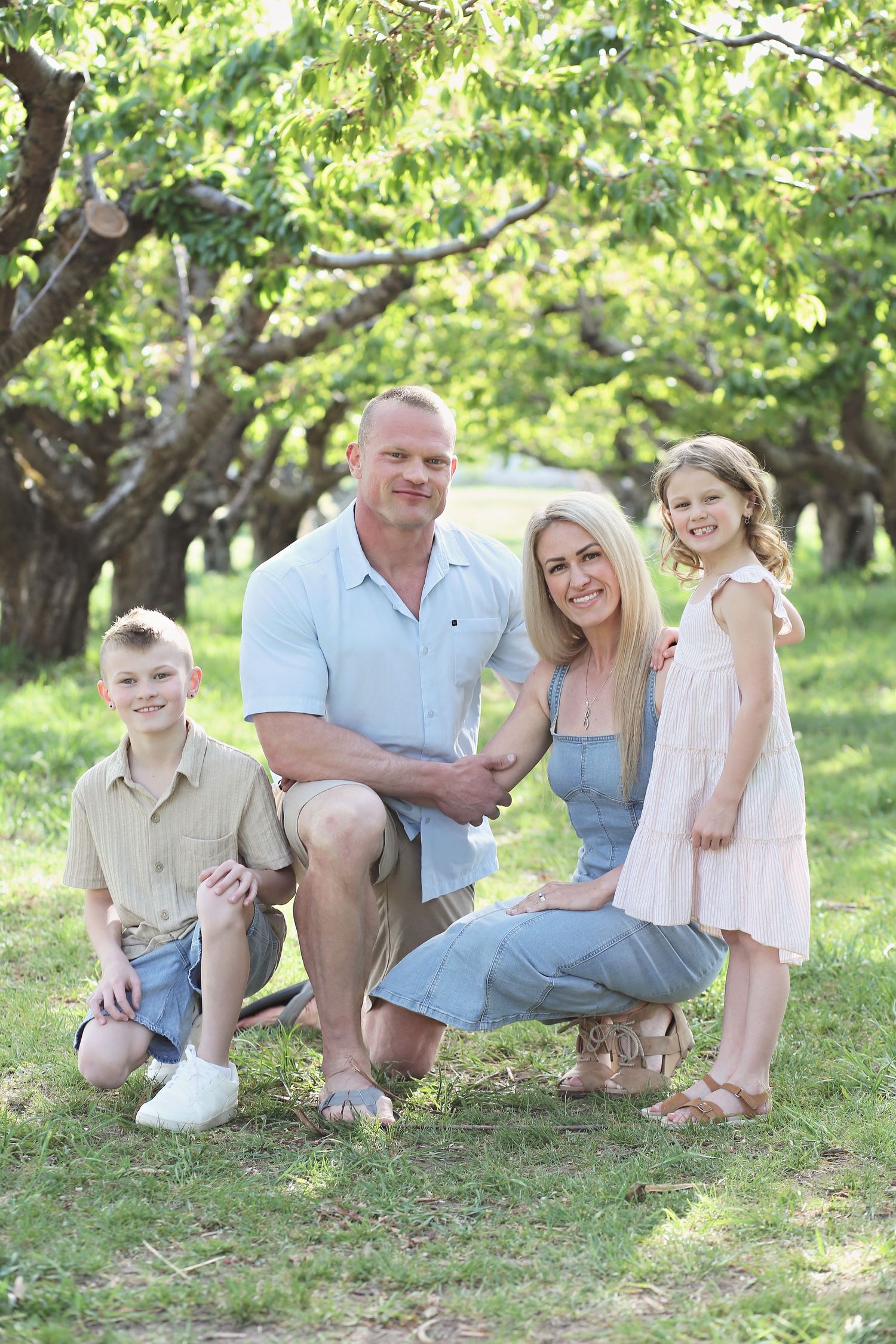 Family group lounging together on grass under blooming trees in an orchard setting.