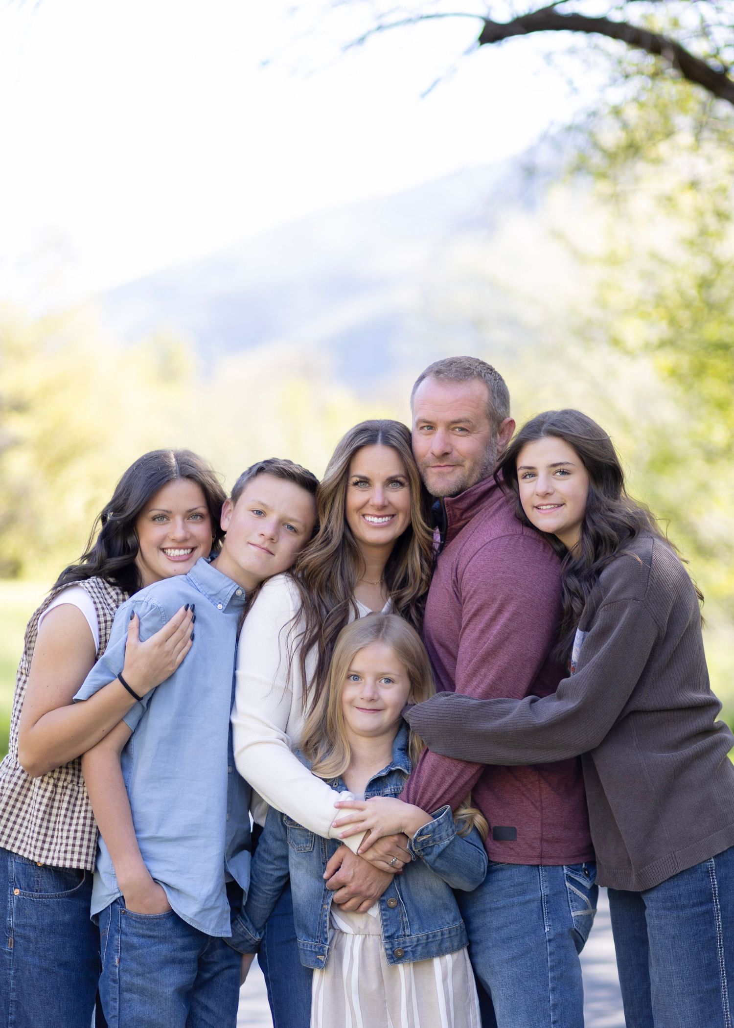 Happy family of six posing outdoors with mountains and trees in the background during a fall portrait session.