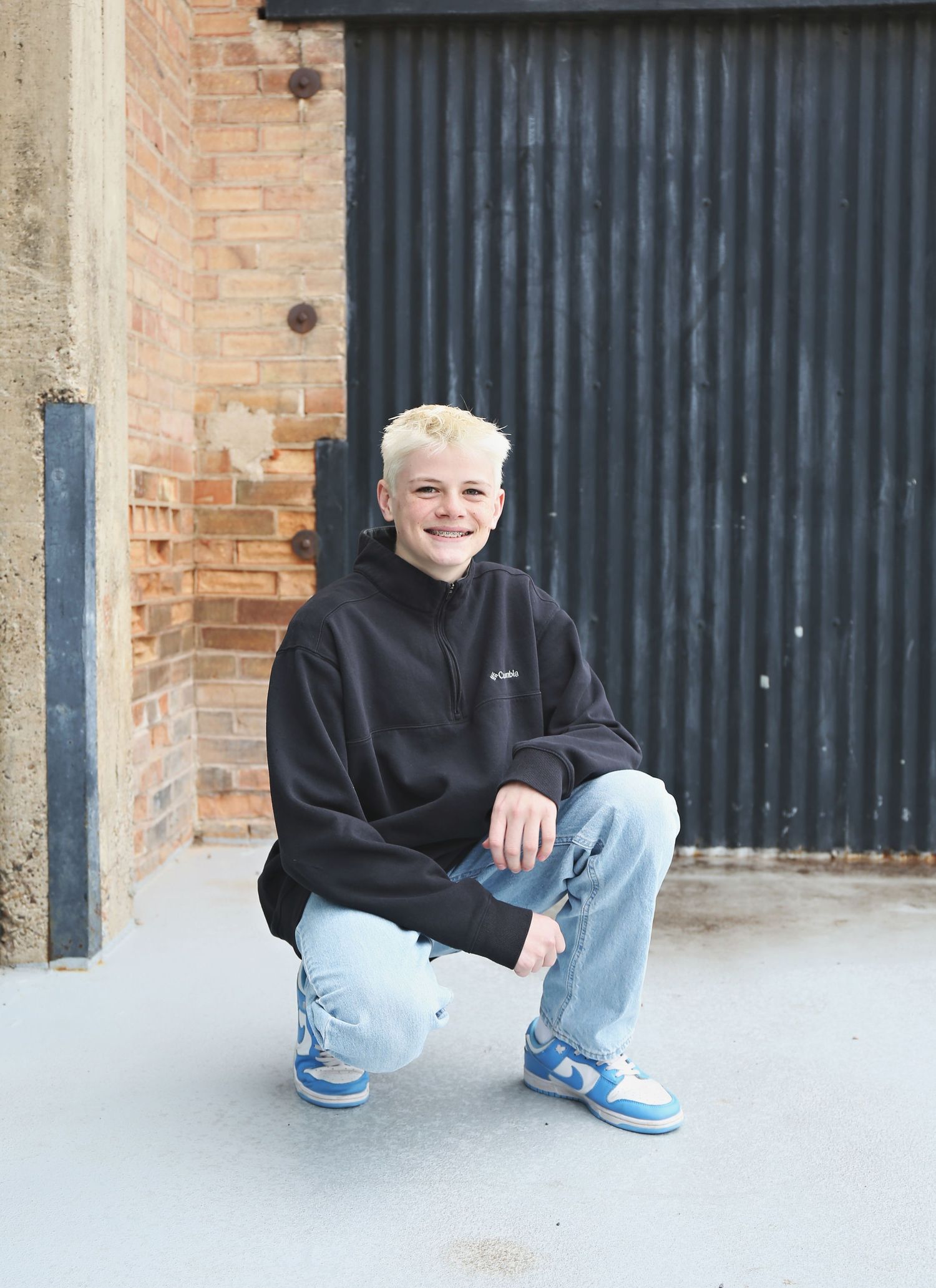 A casual portrait in a black hoodie and jeans against an industrial background.
