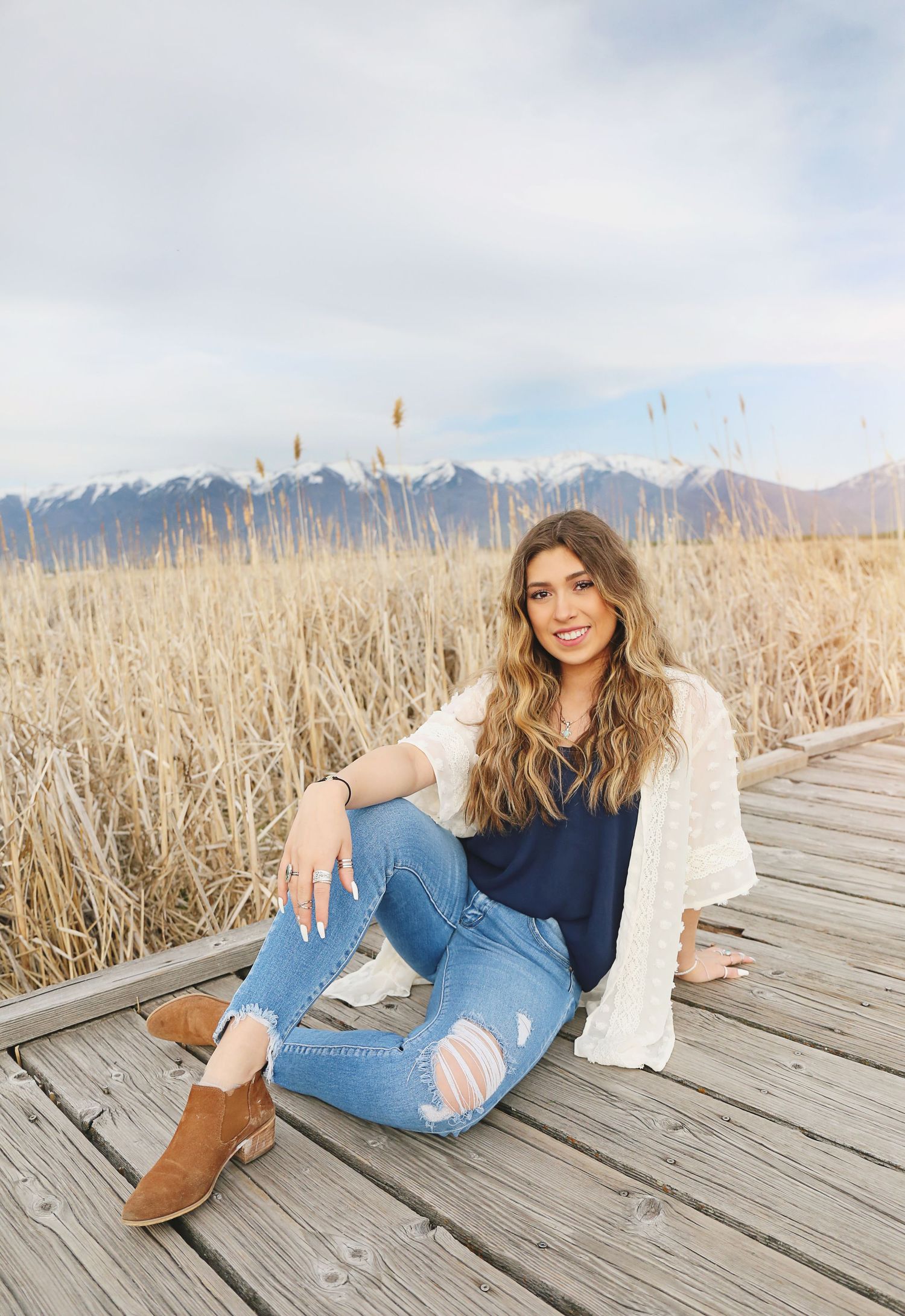 Casual denim and boots outfit styled against mountain backdrop on wooden dock.