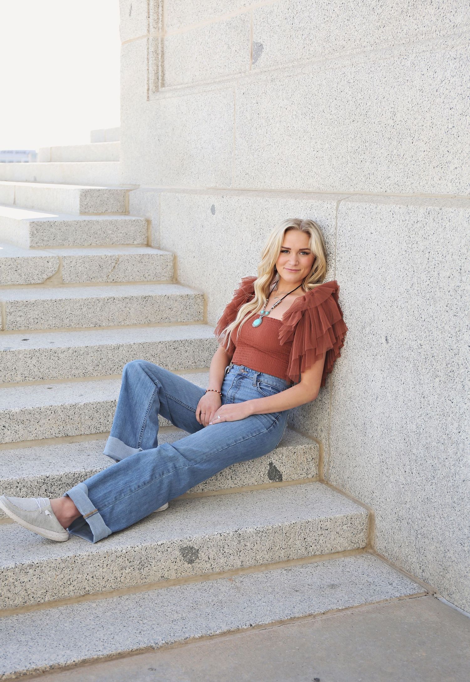 Person in rust-colored top and jeans lounging on concrete steps in casual pose.