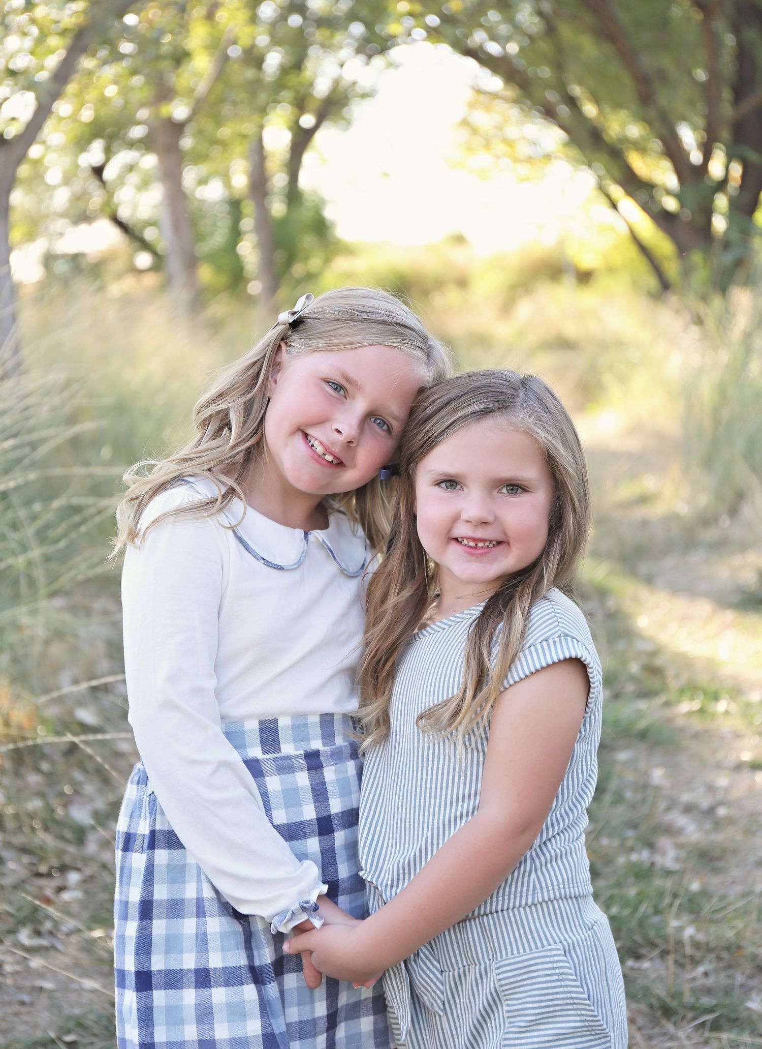 Two young girls in coordinating blue and white dresses hugging outdoors.