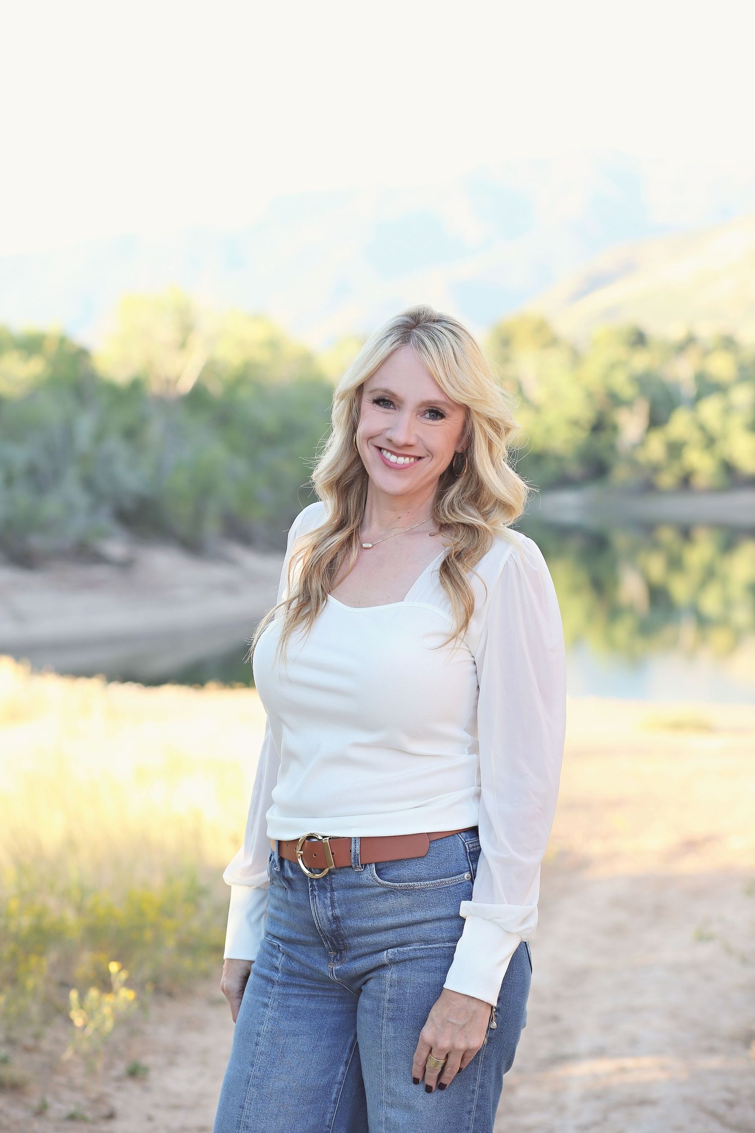 A casual outdoor portrait featuring a white sweater and jeans against a natural landscape.