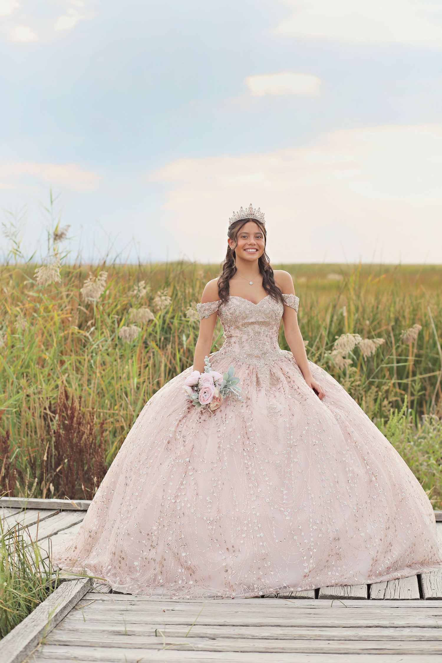 Full pink ballgown with detailed embellishments photographed on wooden deck in natural setting.