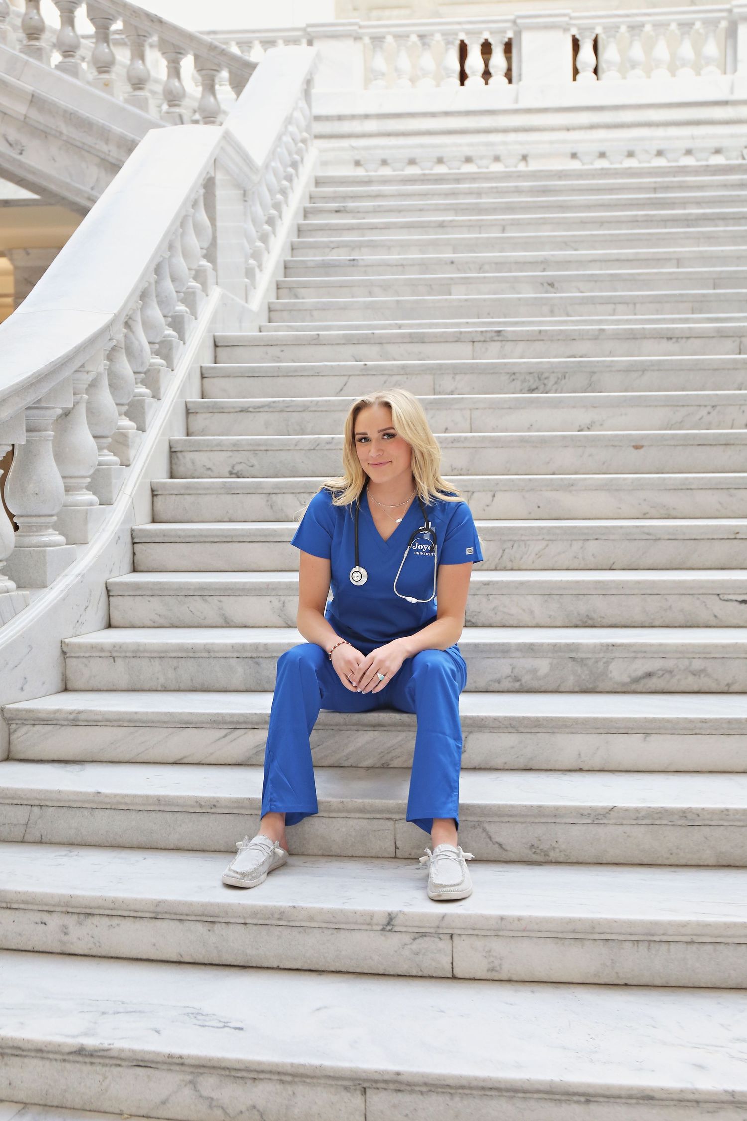 Healthcare professional in blue scrubs sits on white marble steps in a series of candid poses.