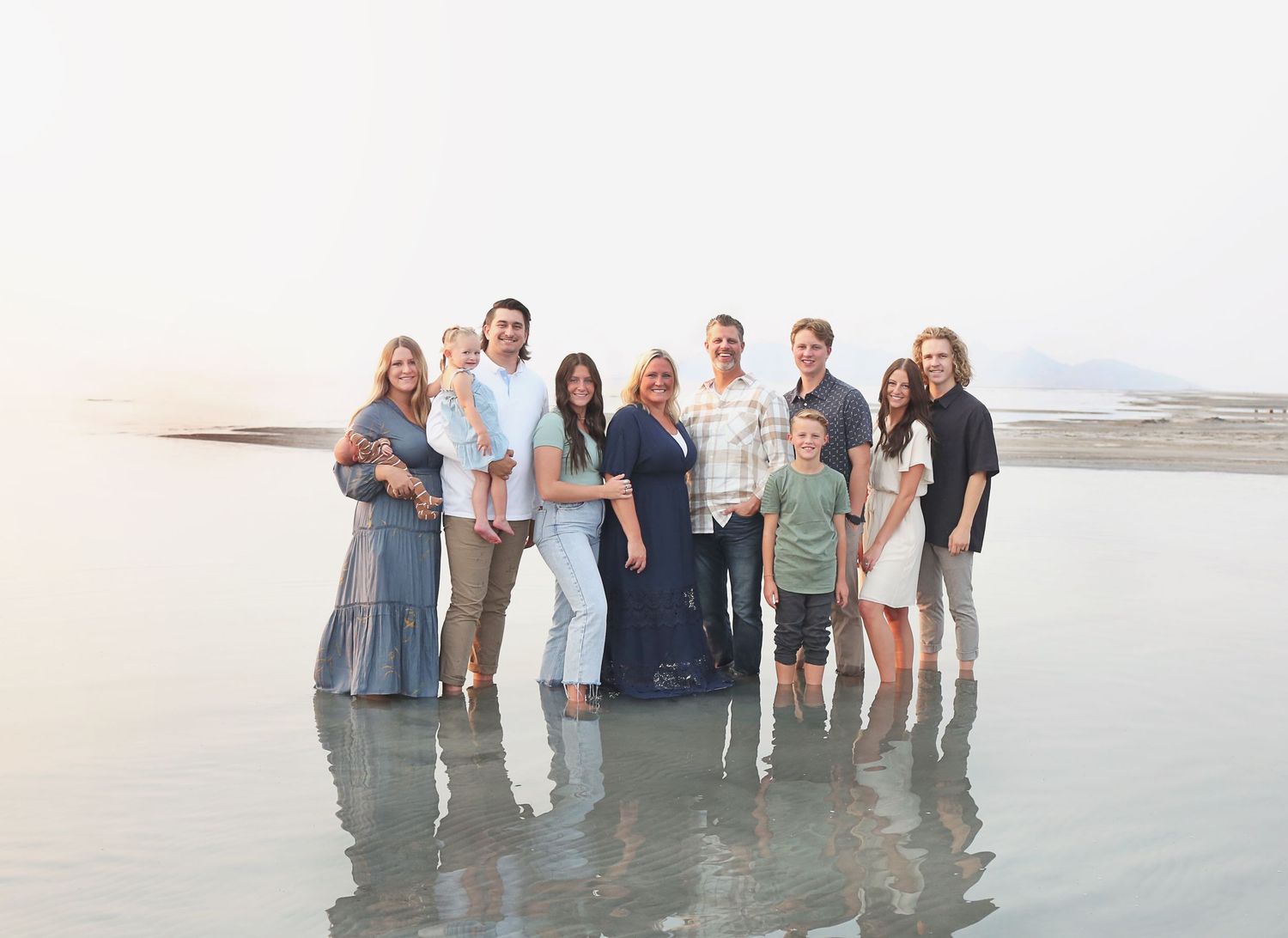 A large group photo of people standing together at the beach during sunset.