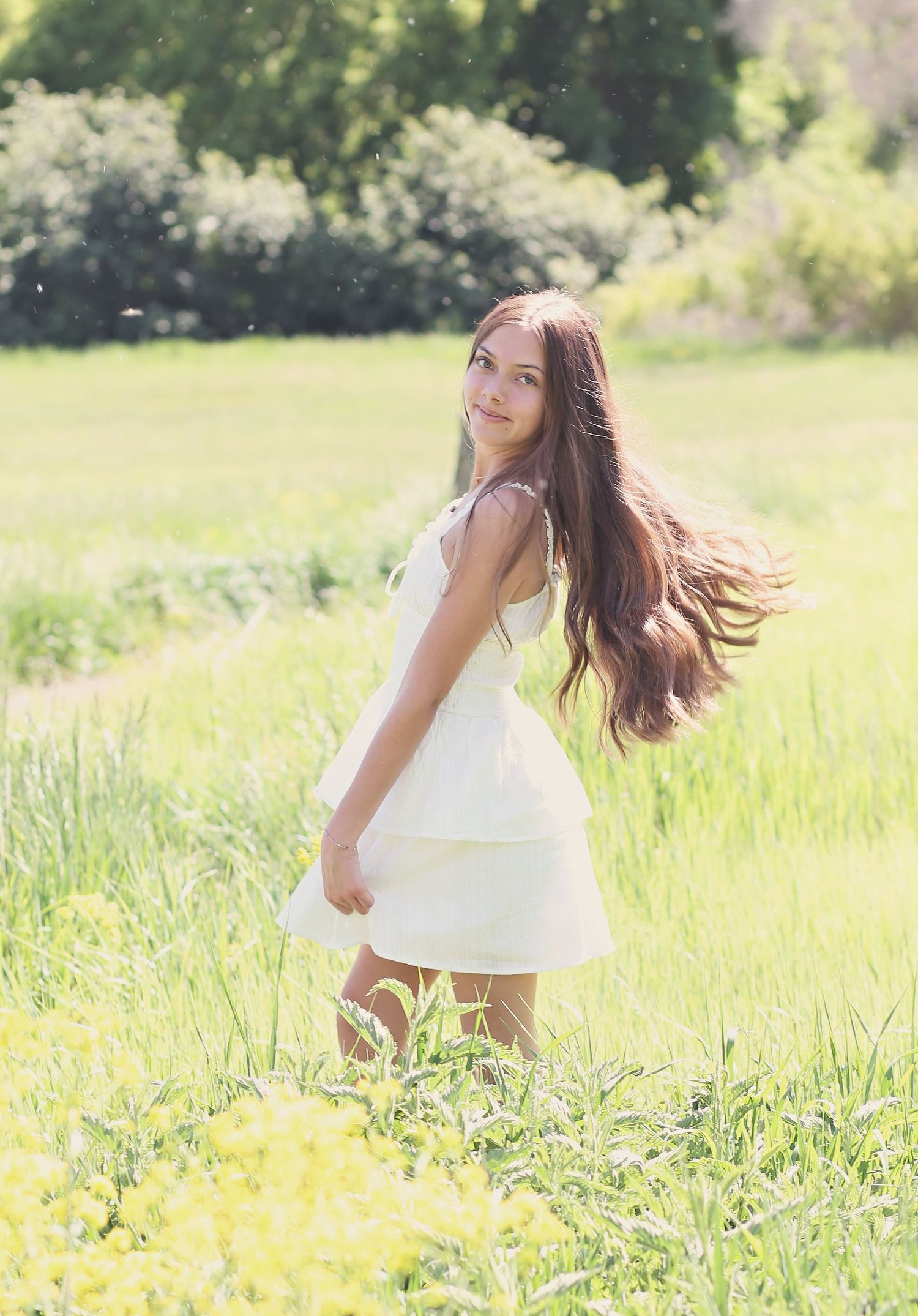 Young person in white dress twirls playfully in a sunny meadow with tall grass.