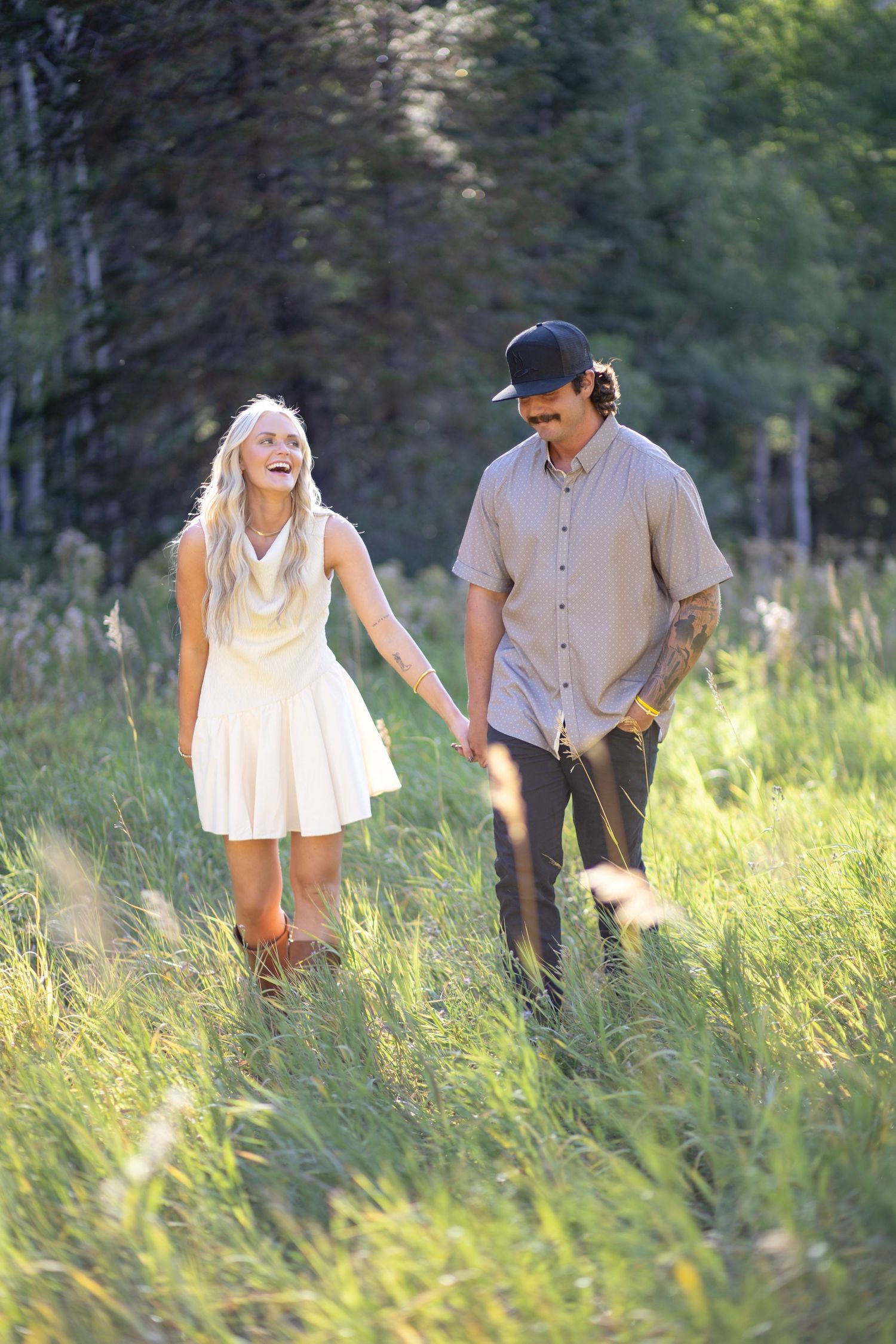 Couple playing and laughing together in tall summer grass with mountain scenery.