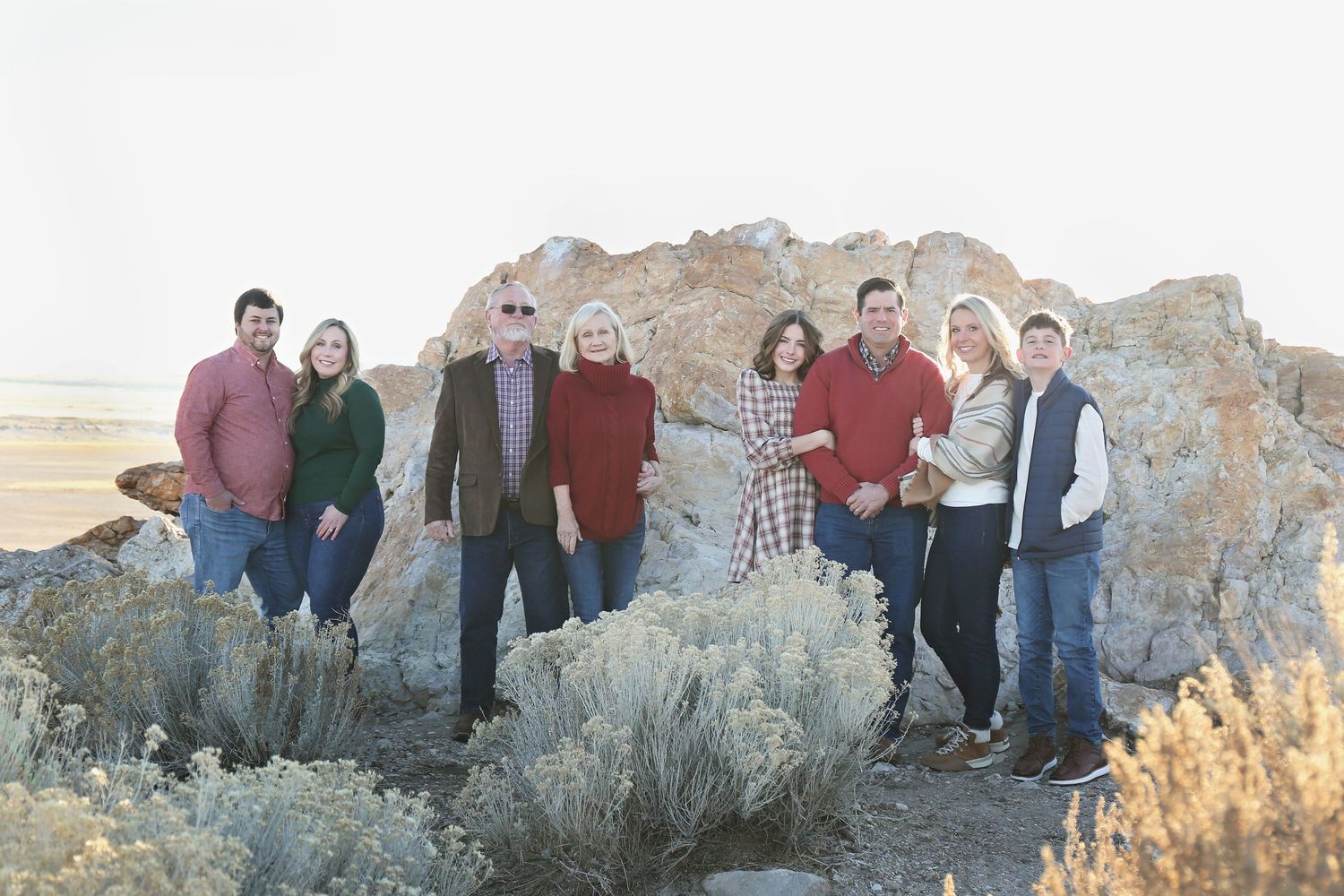 Group poses casually along rocky desert landscape during sunset photo session.