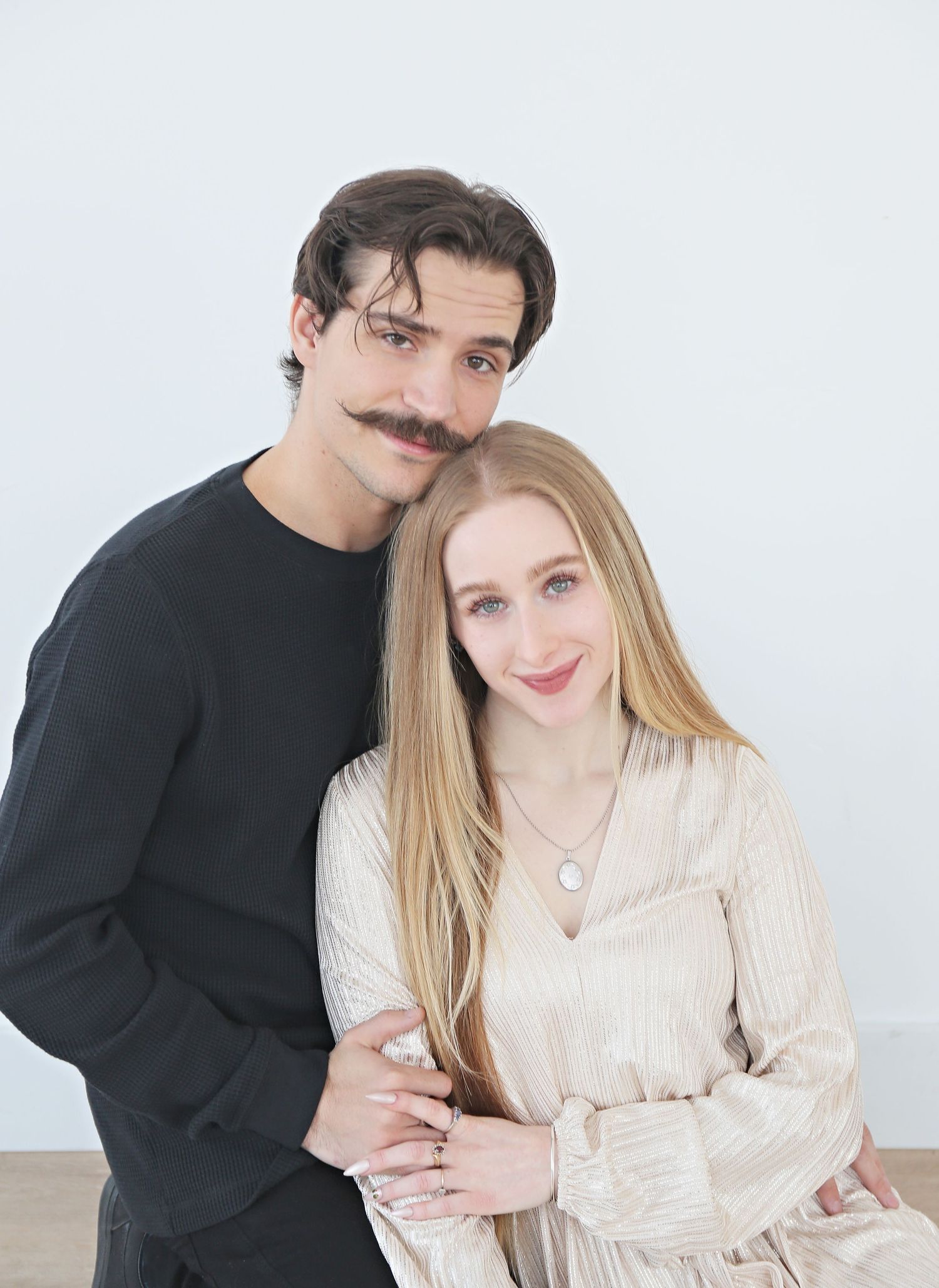 A couple poses together against a white background in contrasting black and cream outfits.