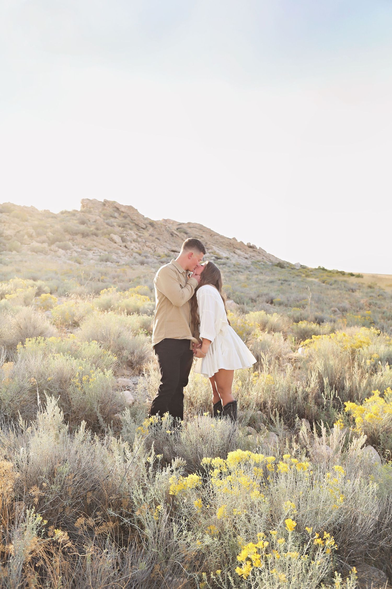 Couple embracing in a desert landscape with sagebrush and mountains in the background.
