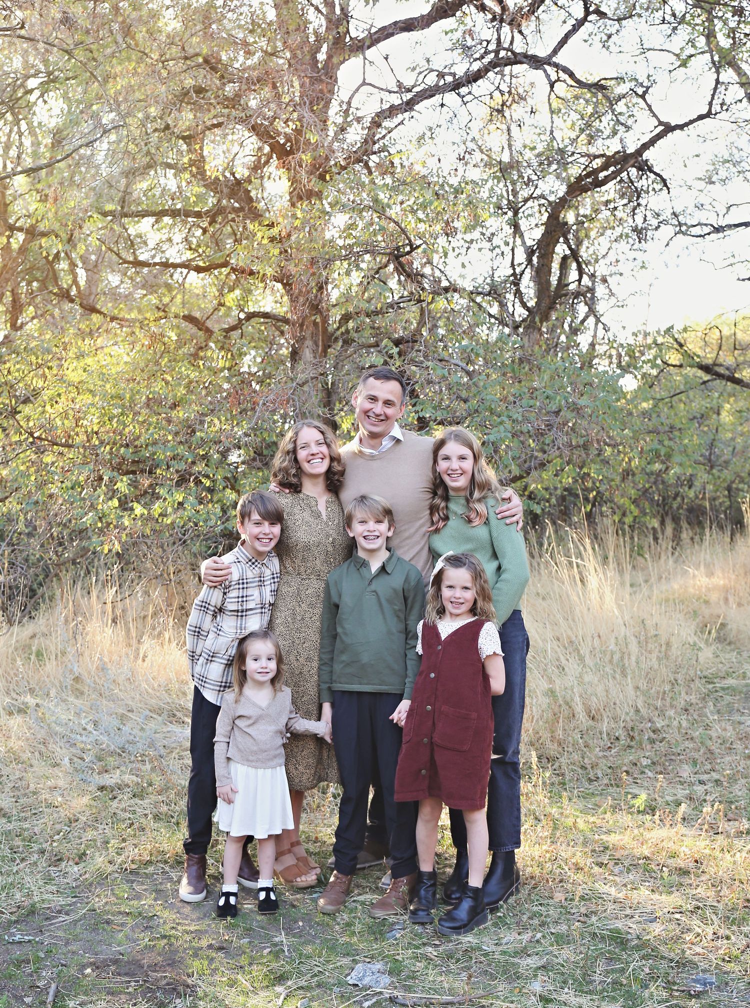 Family portrait of eight people in casual attire standing together outdoors in autumn.