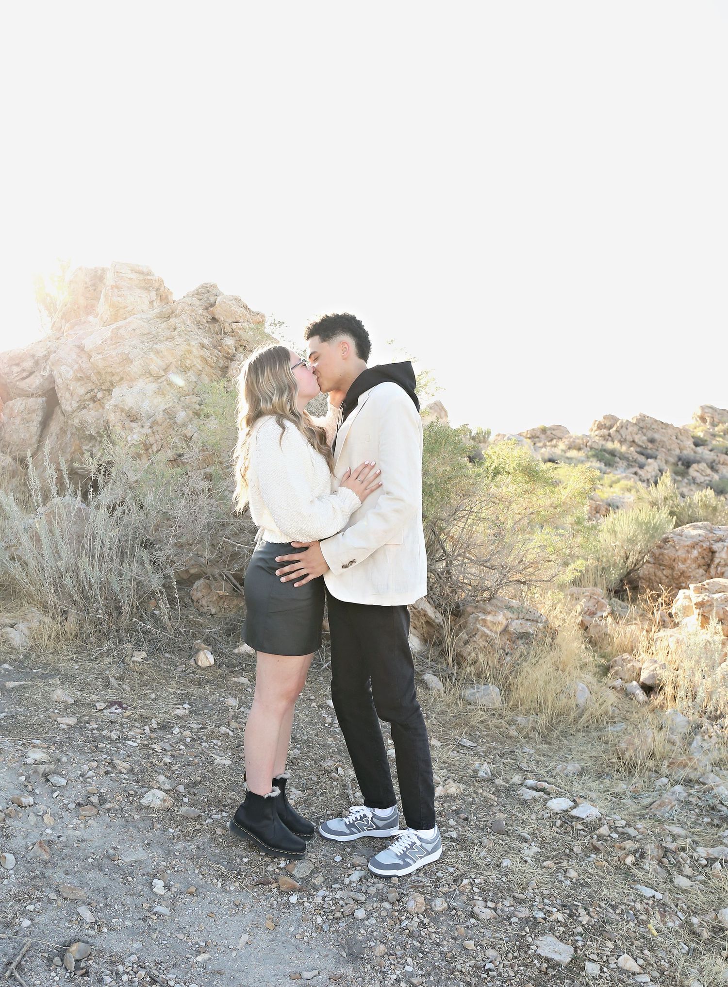 A couple embraces on a rocky desert trail during sunset.