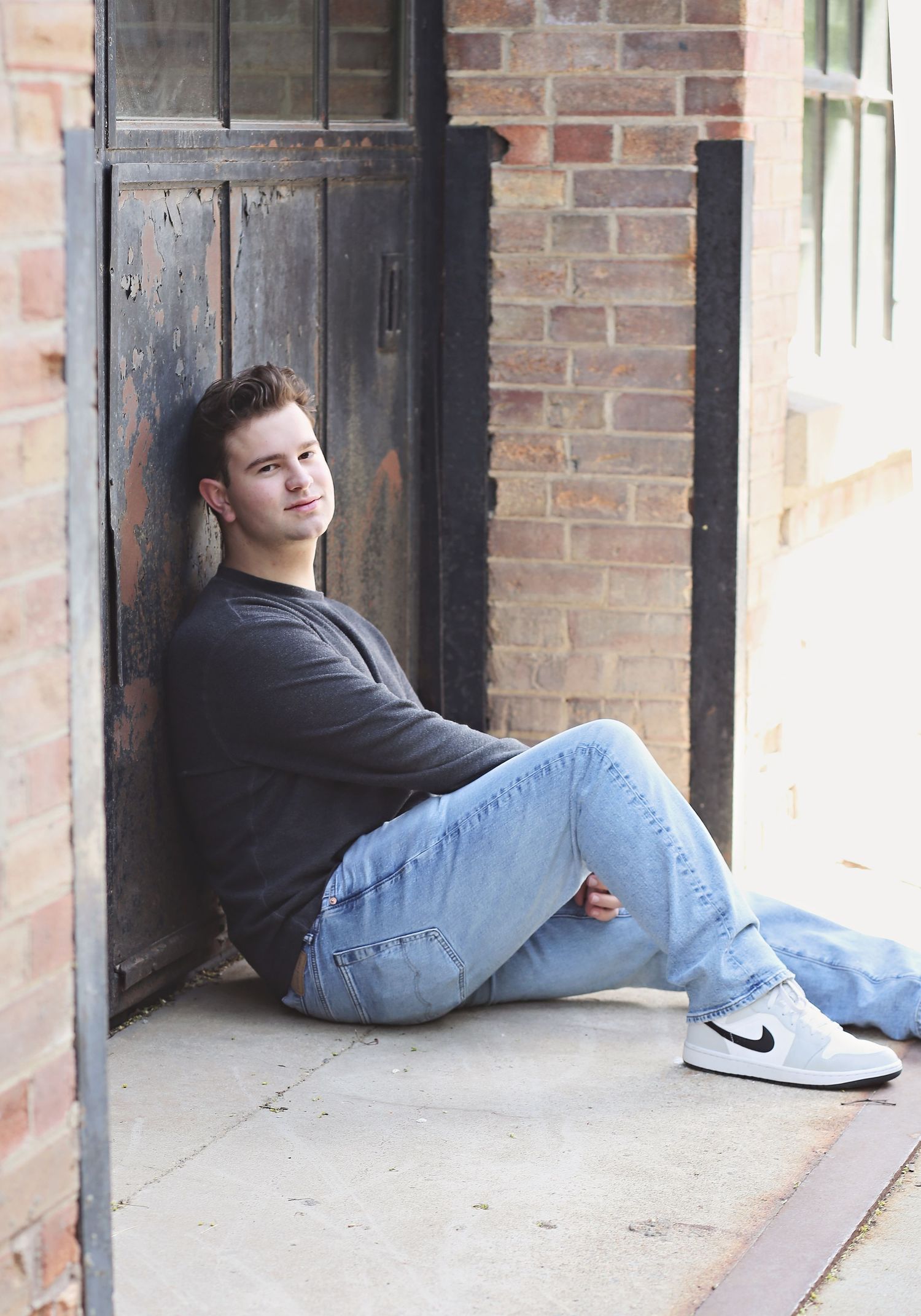 Relaxed pose against vintage wooden door and brick wall.