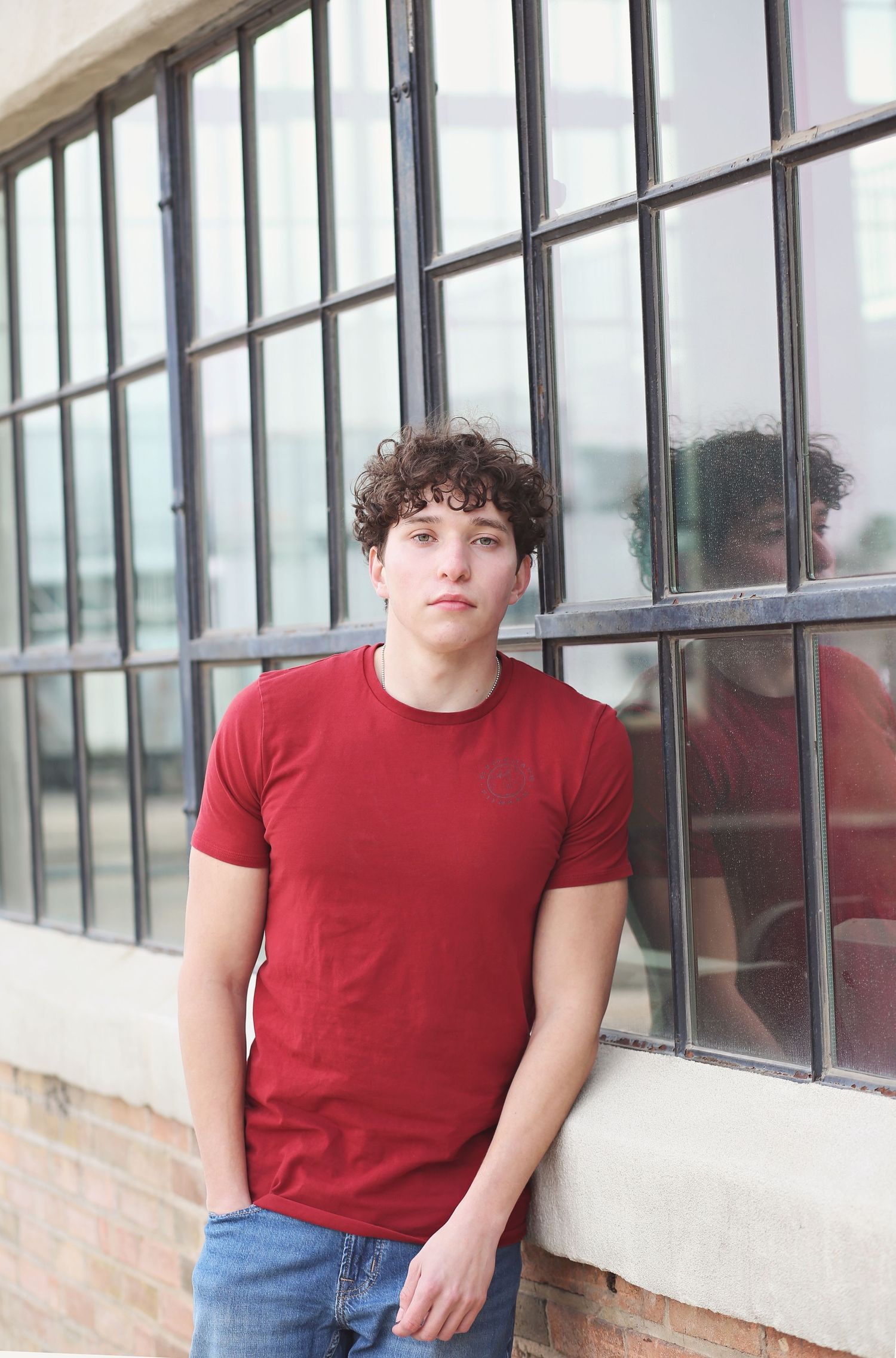 Person in red t-shirt standing by large industrial windows with reflection.