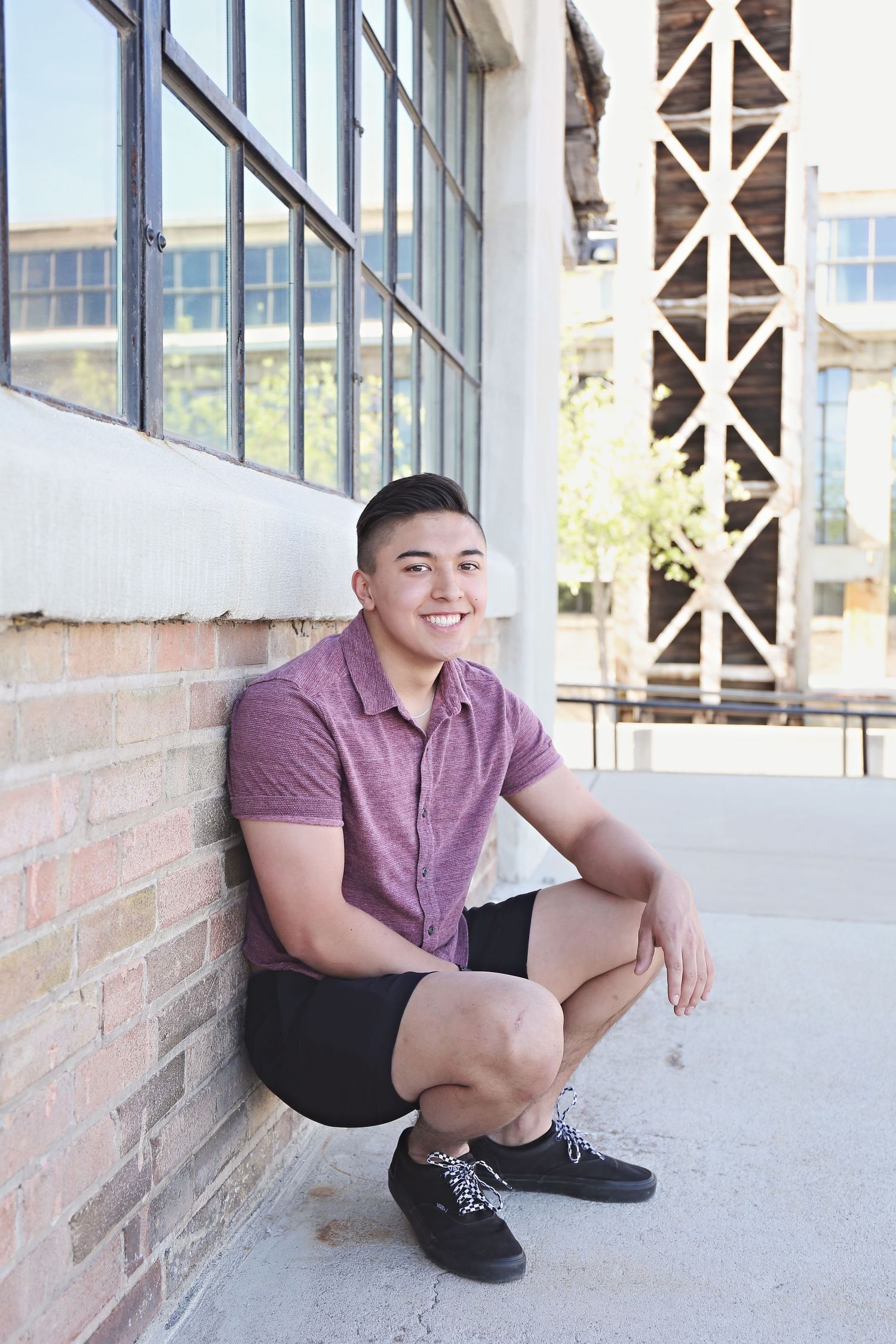 Person in purple shirt sitting casually against brick wall in sunlit area.