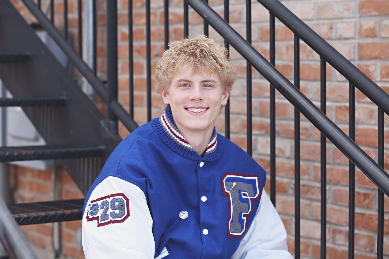 A person in a varsity jacket stands by brick stairs during an outdoor photo session.