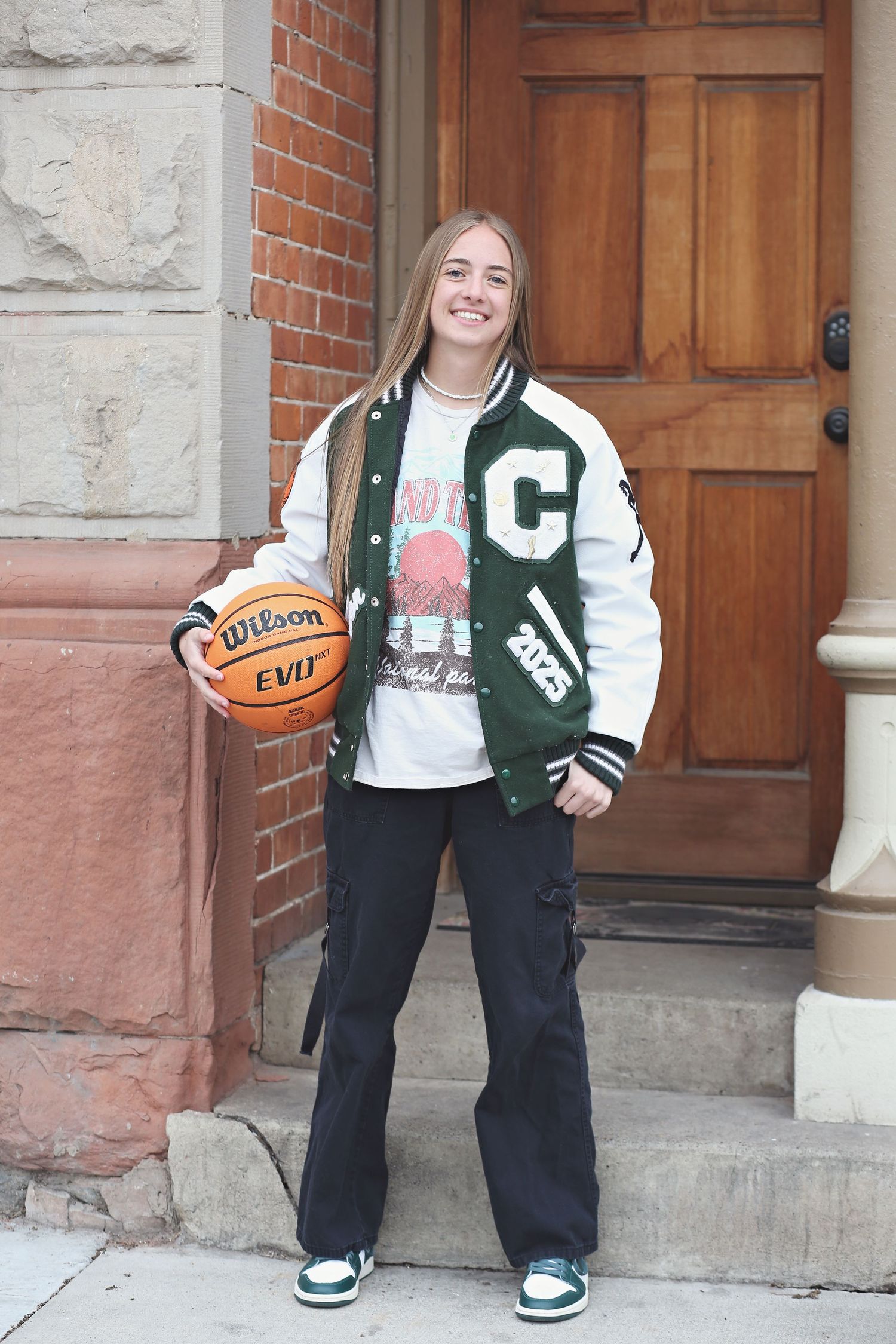 Sports-themed portrait with varsity jacket and basketball against brick and wooden doorway.