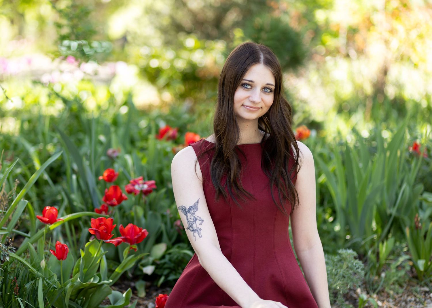 Young woman in burgundy dress smiling among red tulips in garden.