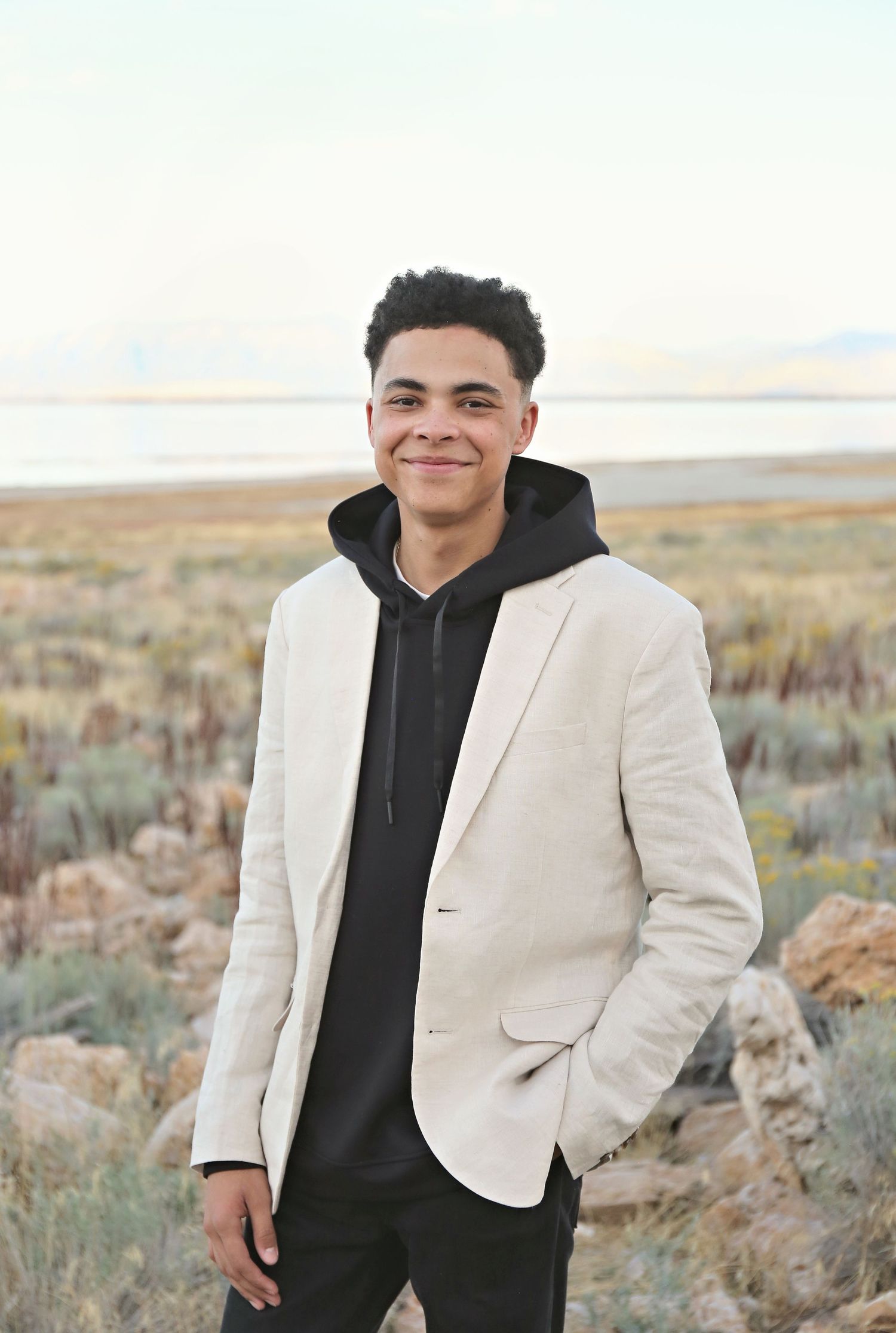 Stylish black hoodie and white blazer combination photographed in desert landscape setting.
