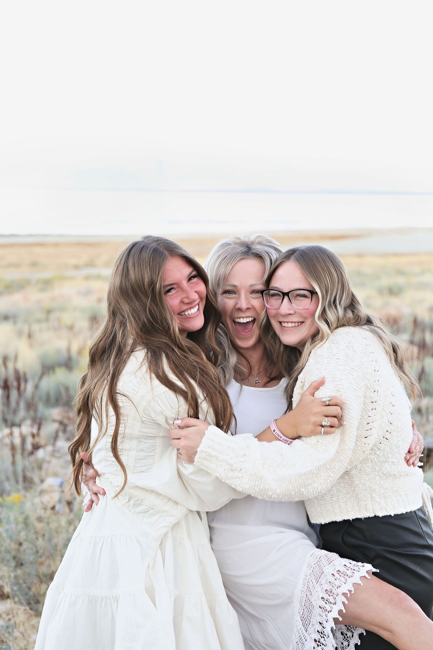 Group of people in white outfits sharing joyful embraces against desert landscape.