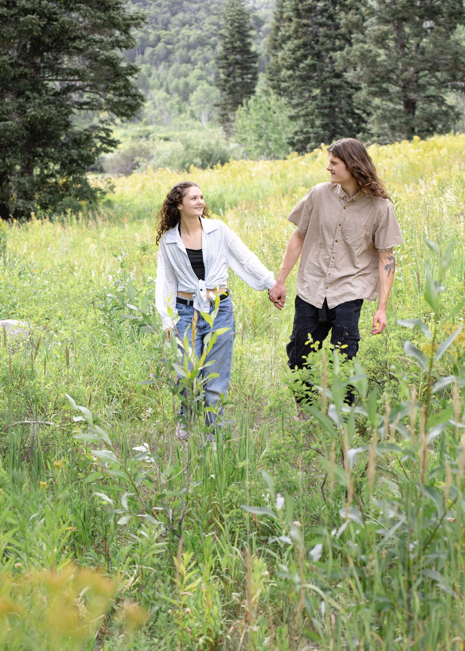 Couple walking through wildflower meadow with mountain landscape in background.