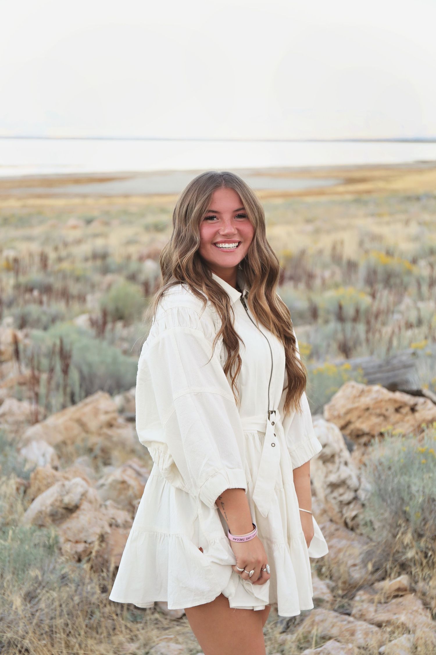 A white flowy dress stands out against a desert landscape with sagebrush and rocky terrain.