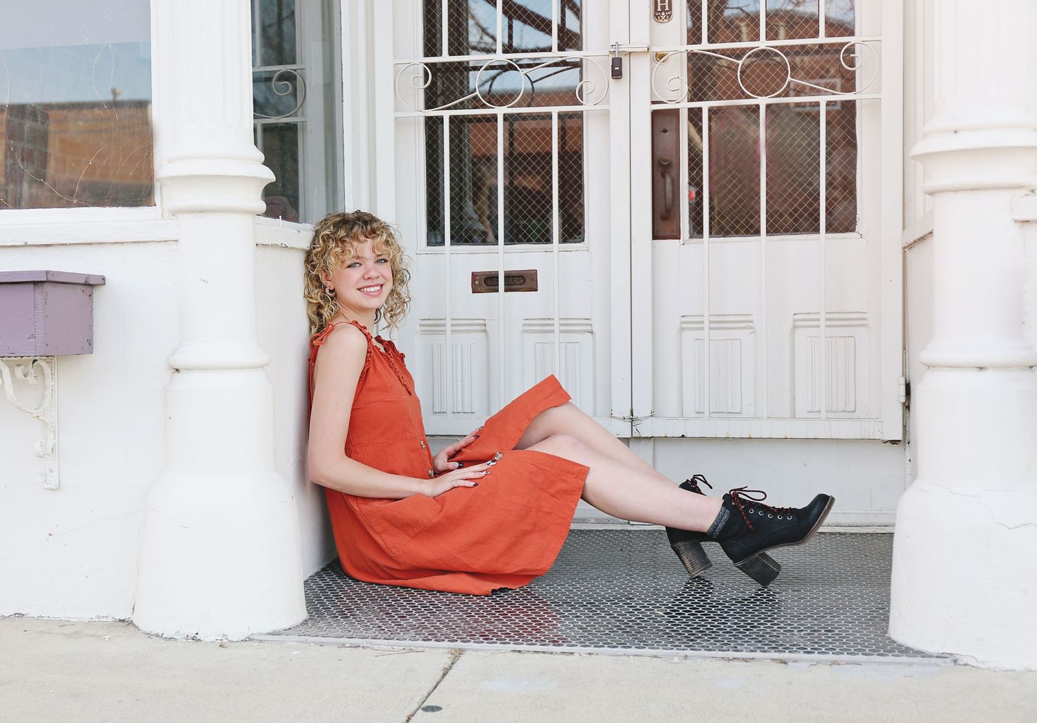 Person in coral dress relaxes on white porch steps in casual outdoor setting.