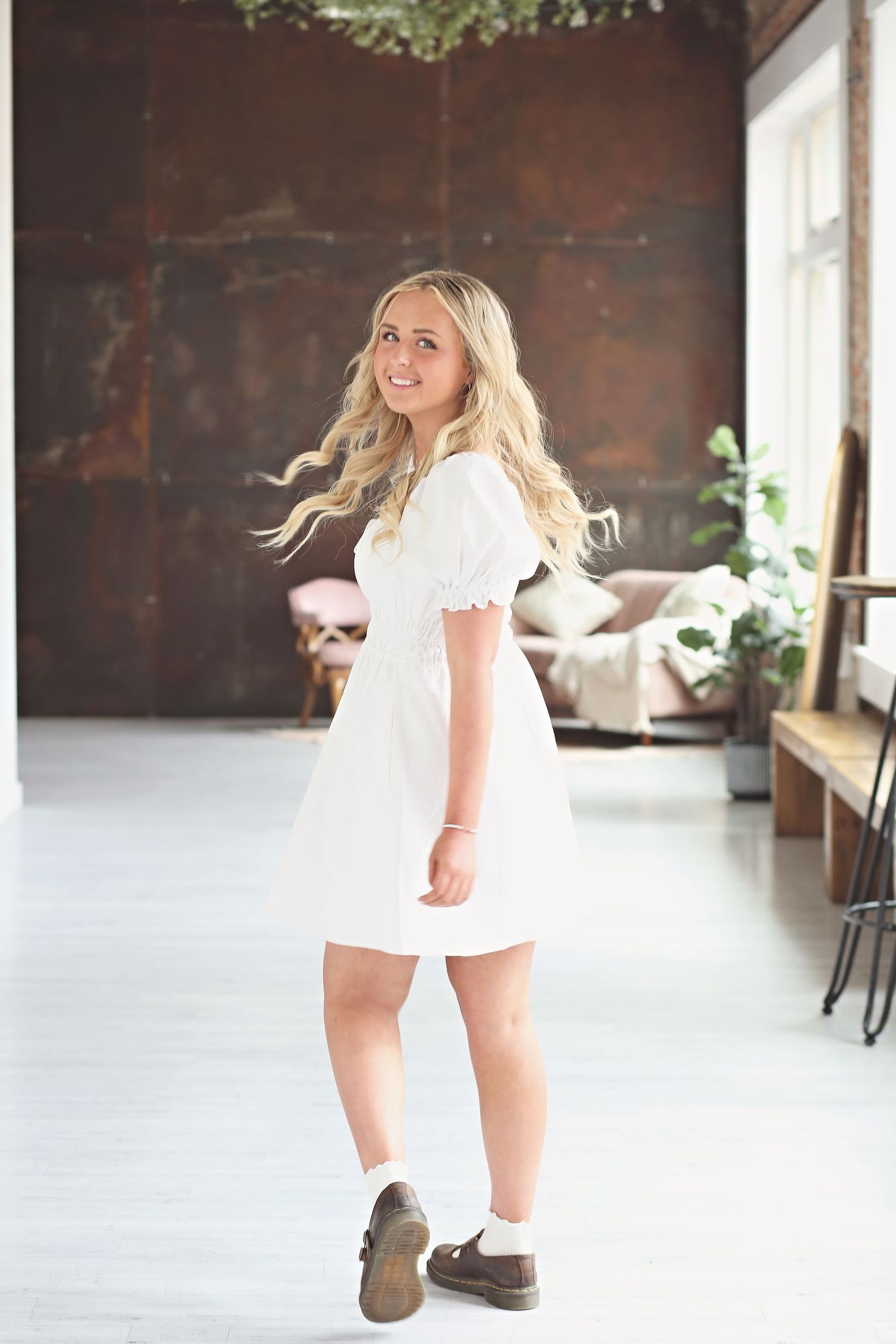 Playful indoor portraits in white dress against industrial brick backdrop.