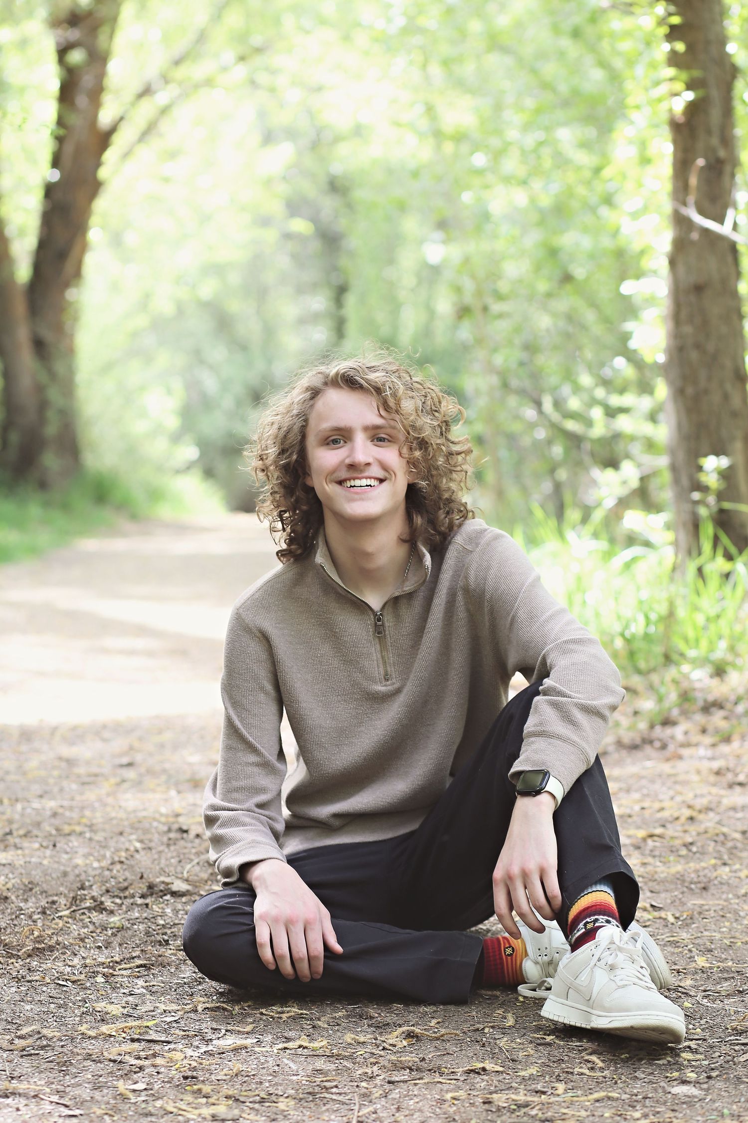 Casual portrait on forest path wearing neutral toned pullover and dark pants.