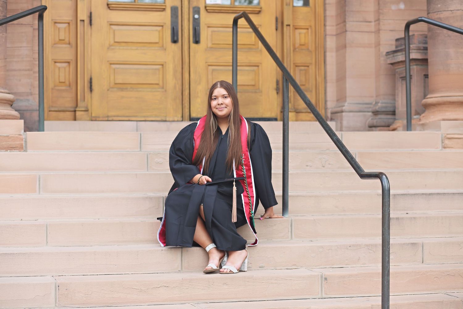 Graduate sitting on stone steps in front of historic university building entrance.