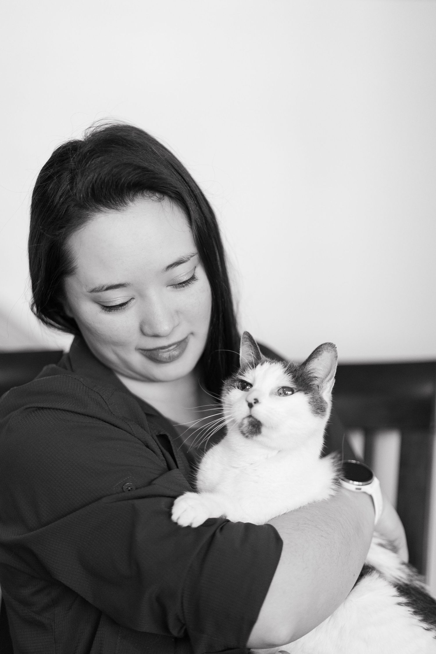 Woman smiling while holding a black and white cat in a black and white portrait photo.