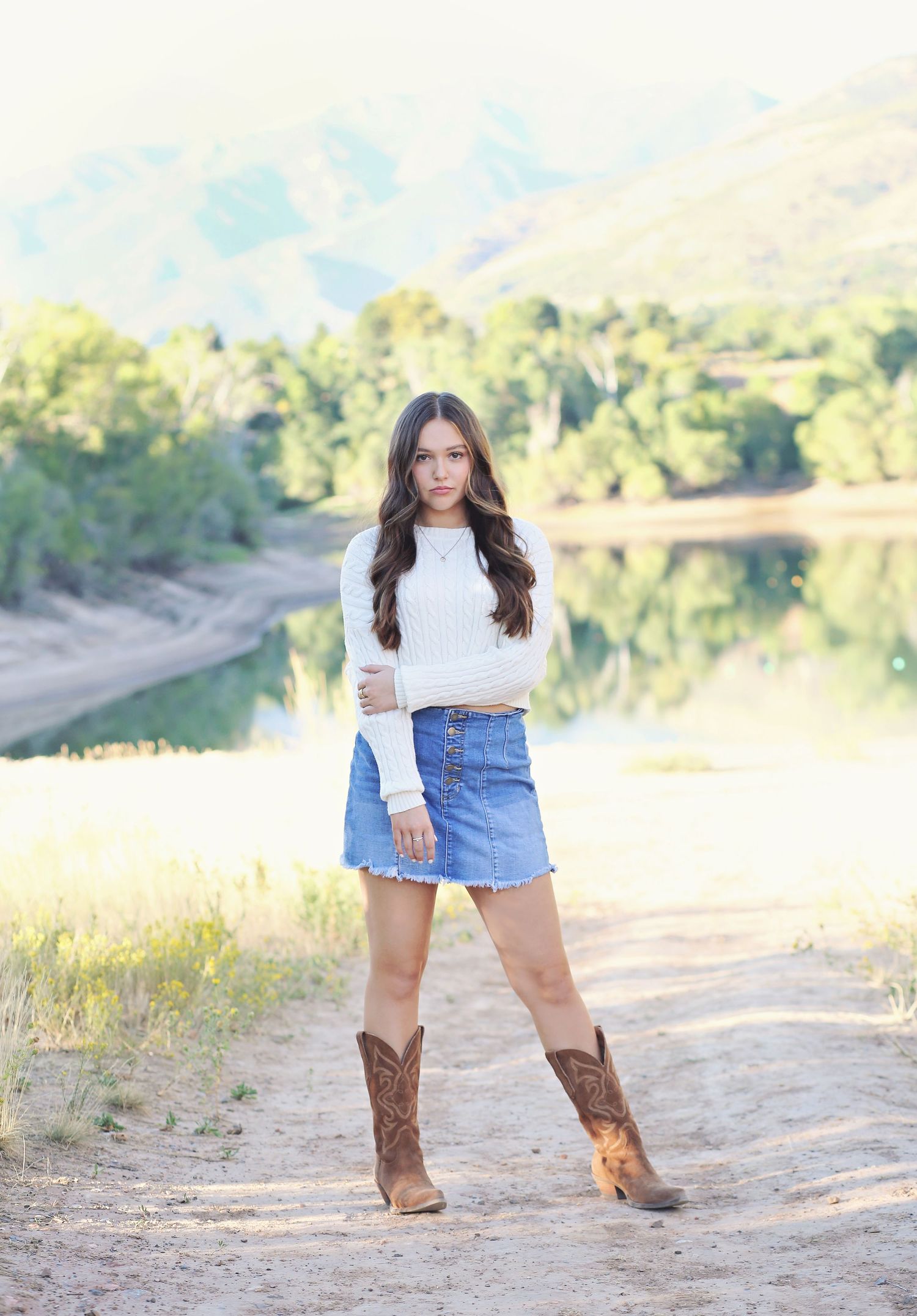 Western style portrait with cowboy boots against scenic lake and mountain backdrop.
