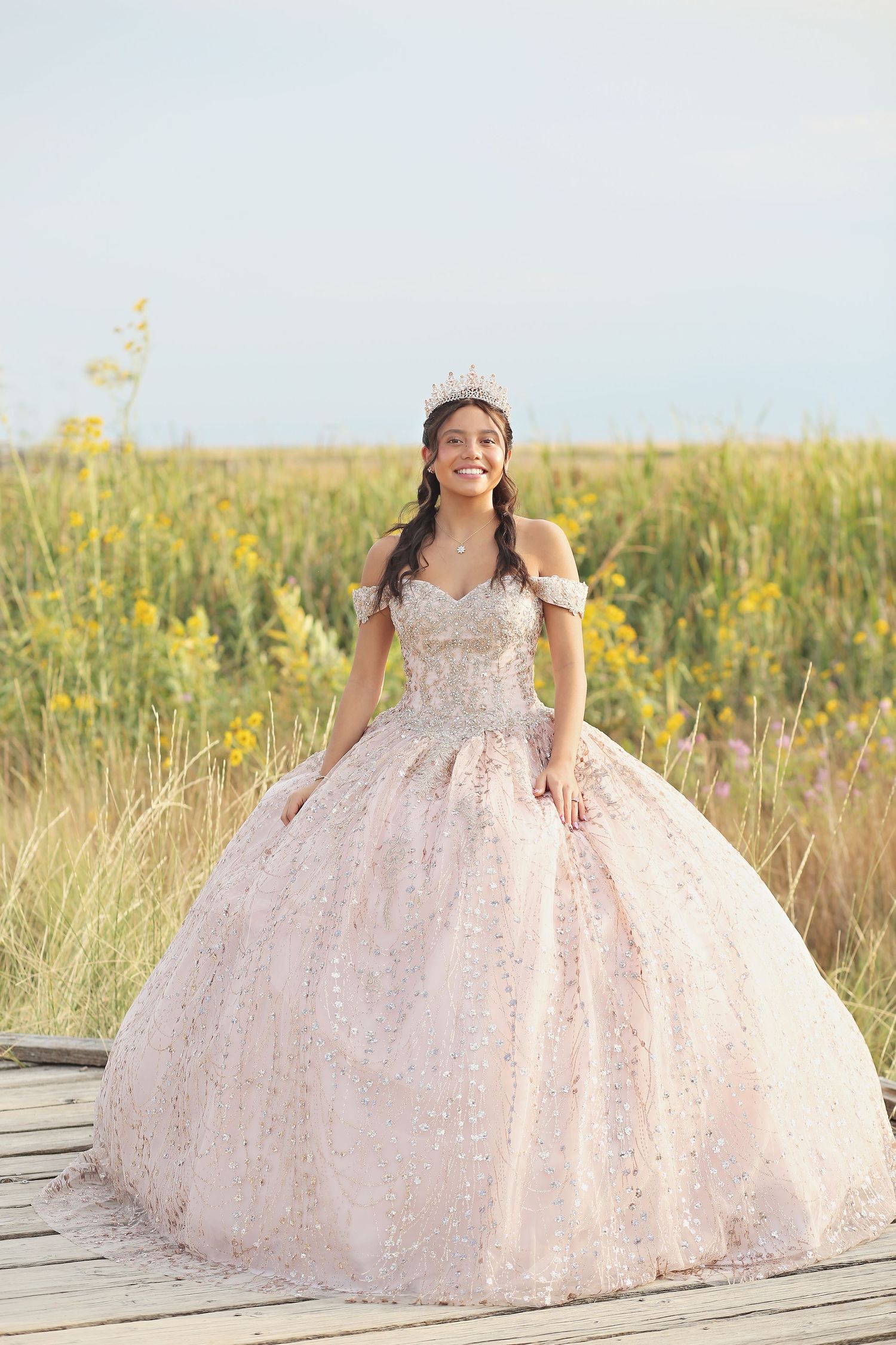 Elegant pink ballgown with sparkles photographed in outdoor field with yellow wildflowers.