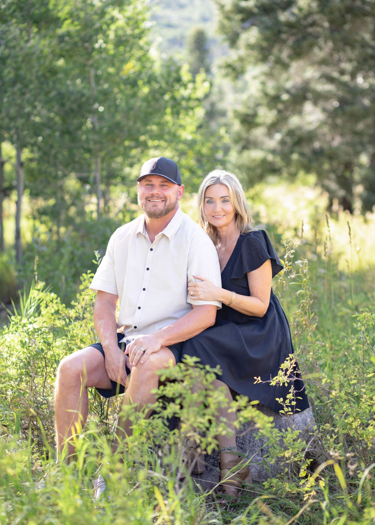 Romantic couple sitting together in a sunny meadow surrounded by tall grass and wildflowers.