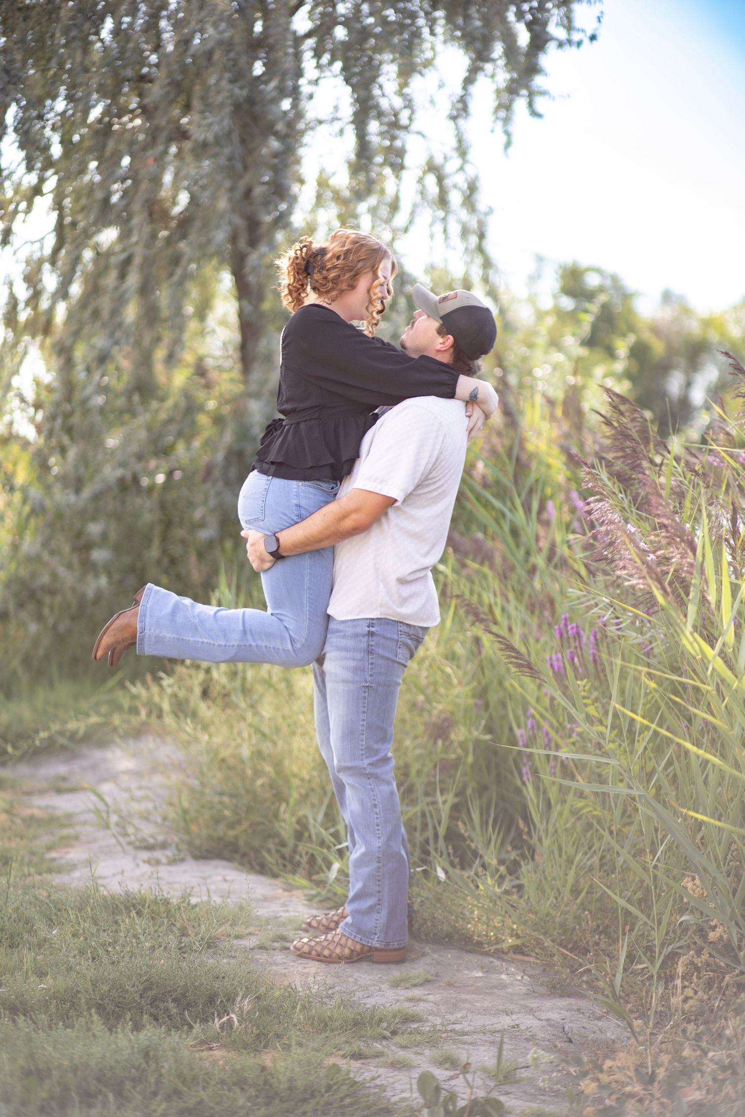 Romantic couple embracing in tall grass during golden hour photoshoot.