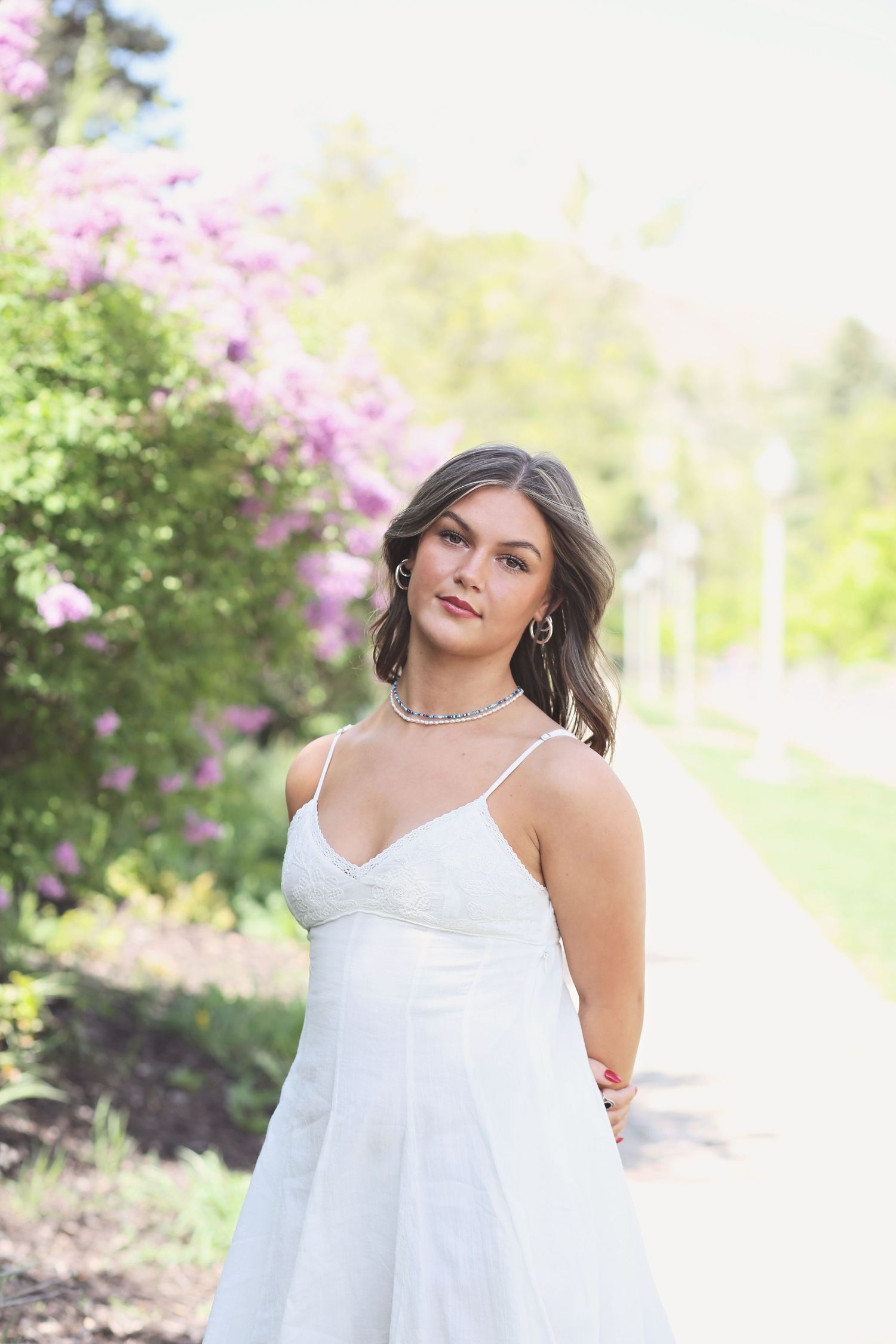 Person in flowing white dress posing in garden setting with pink flowers.