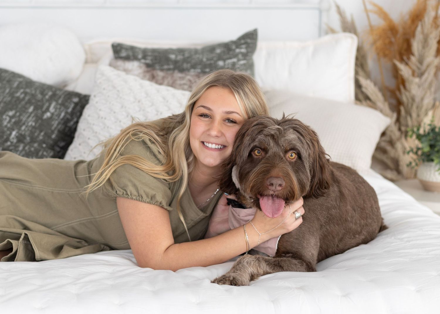 A chocolate lab puppy cuddles on white bedding during an indoor photoshoot.