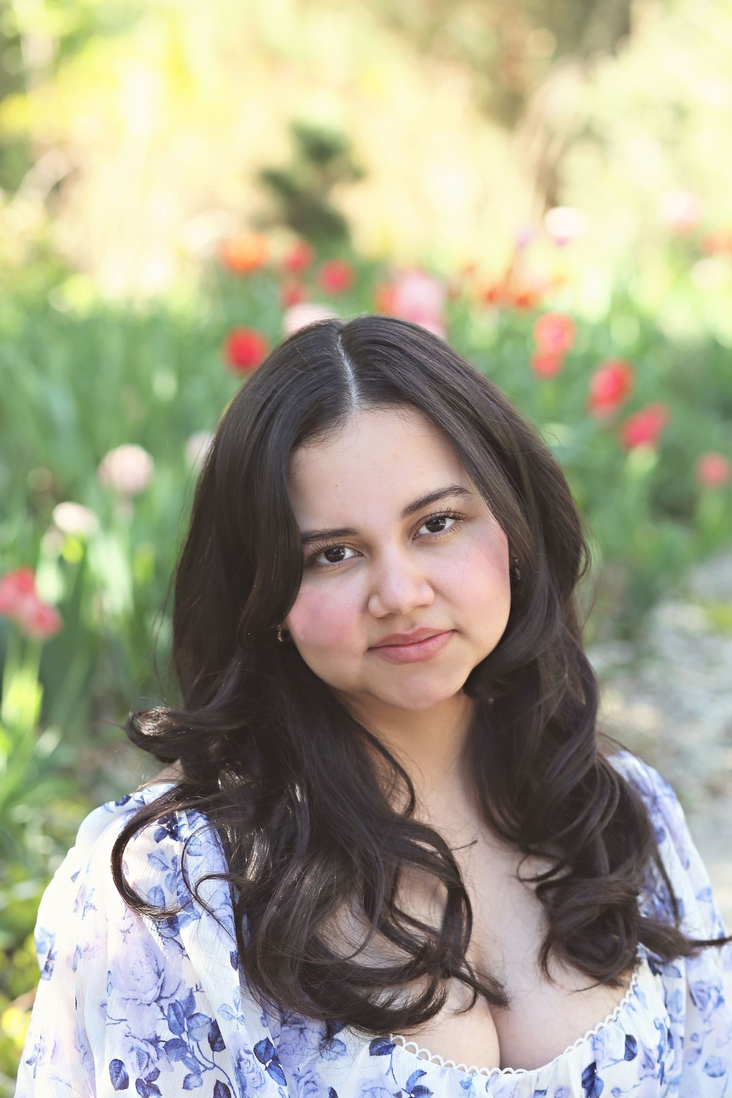 Portrait in garden setting with blooming red flowers and natural sunlight.
