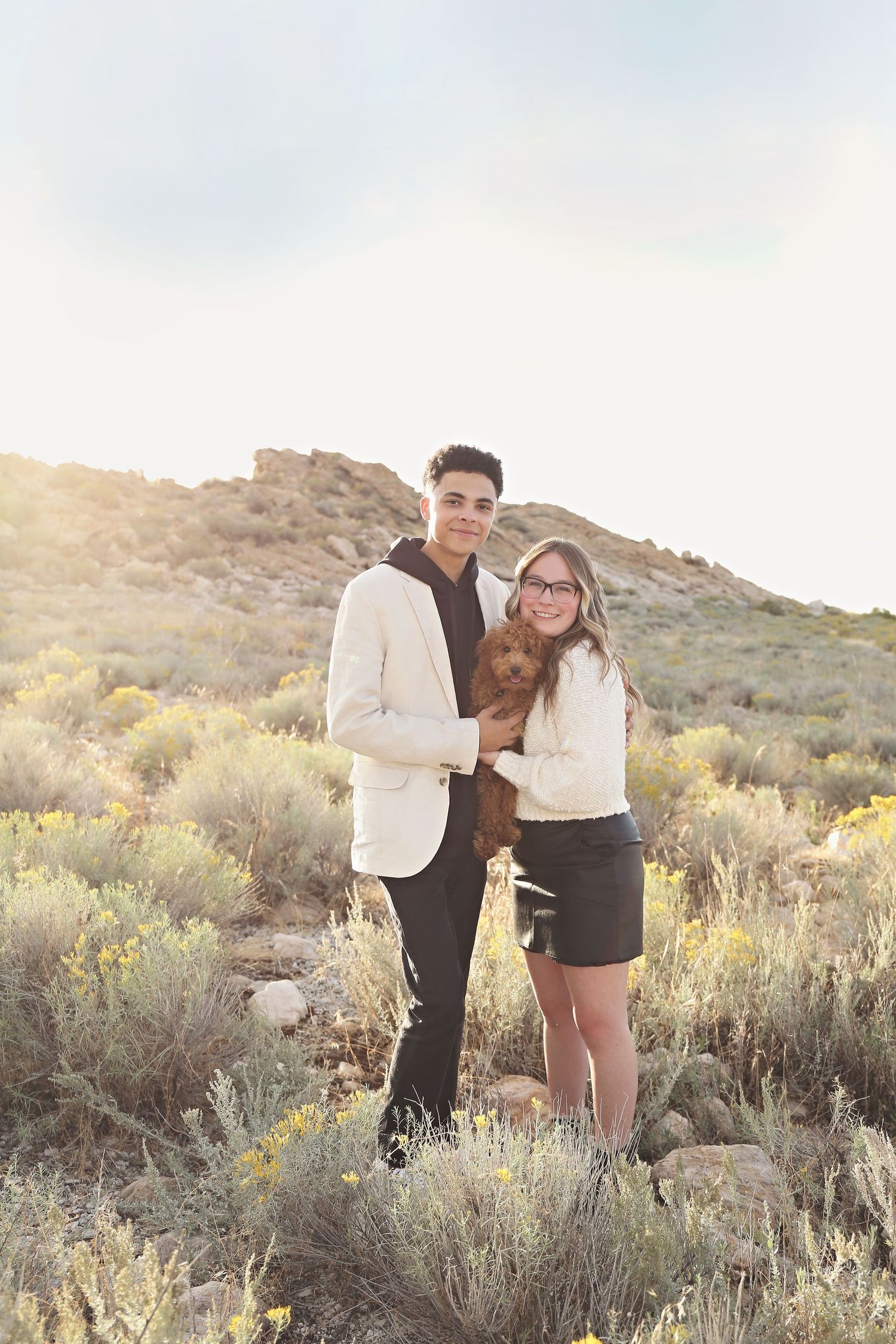 A couple shares a romantic moment among desert brush during golden hour.