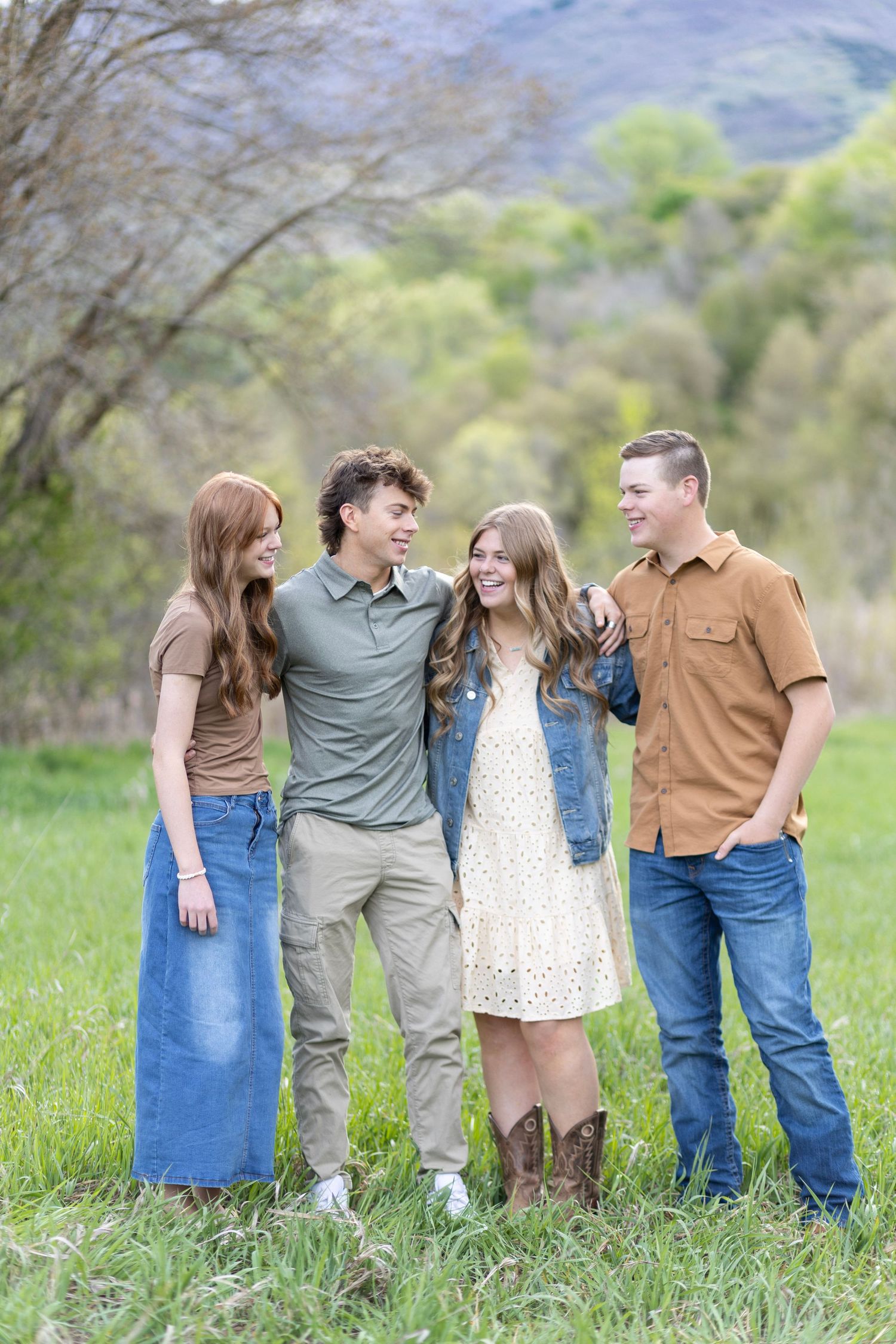 Four young adults laughing and posing together in a green meadow.