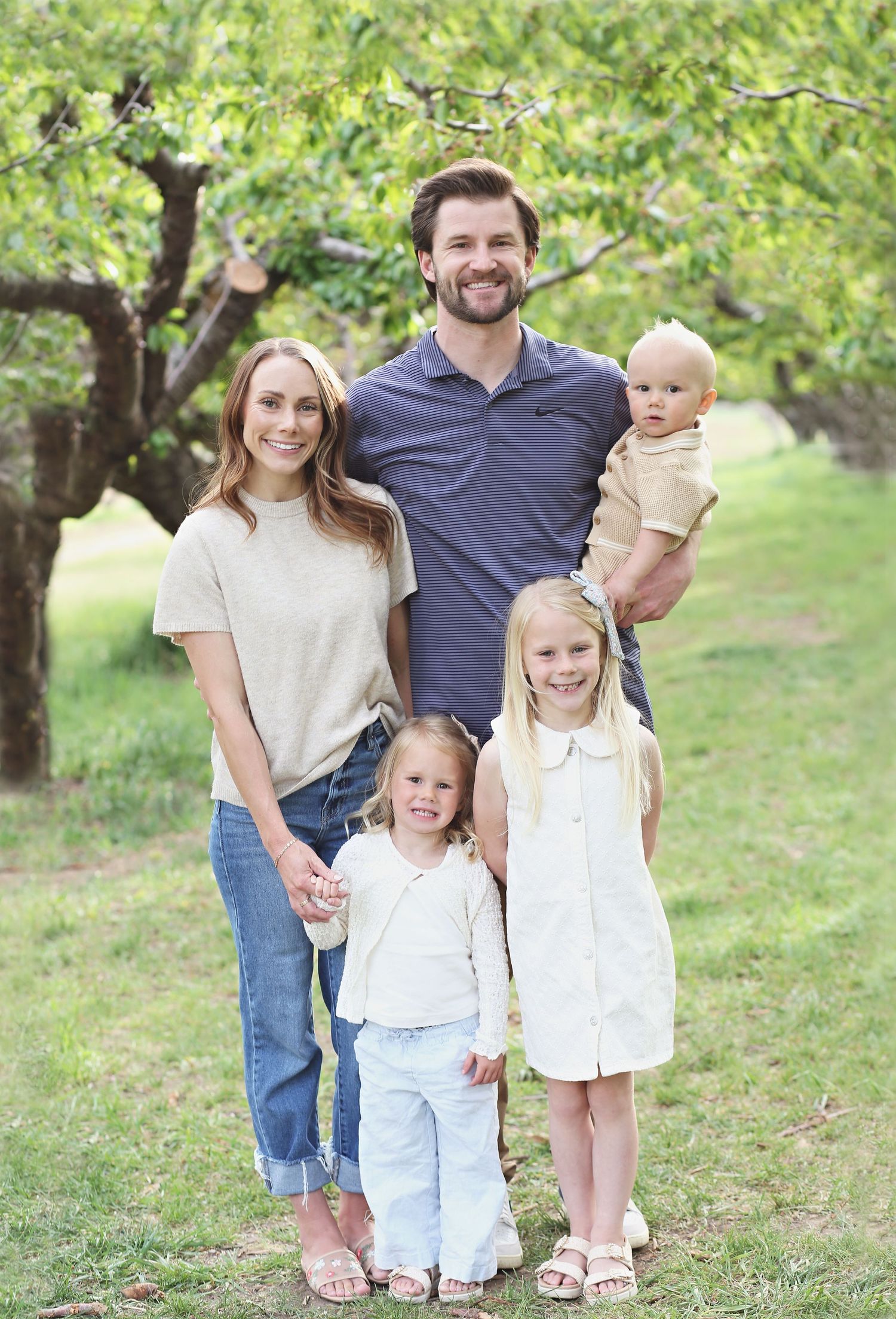 Family portrait session outdoors with everyone smiling under green trees.