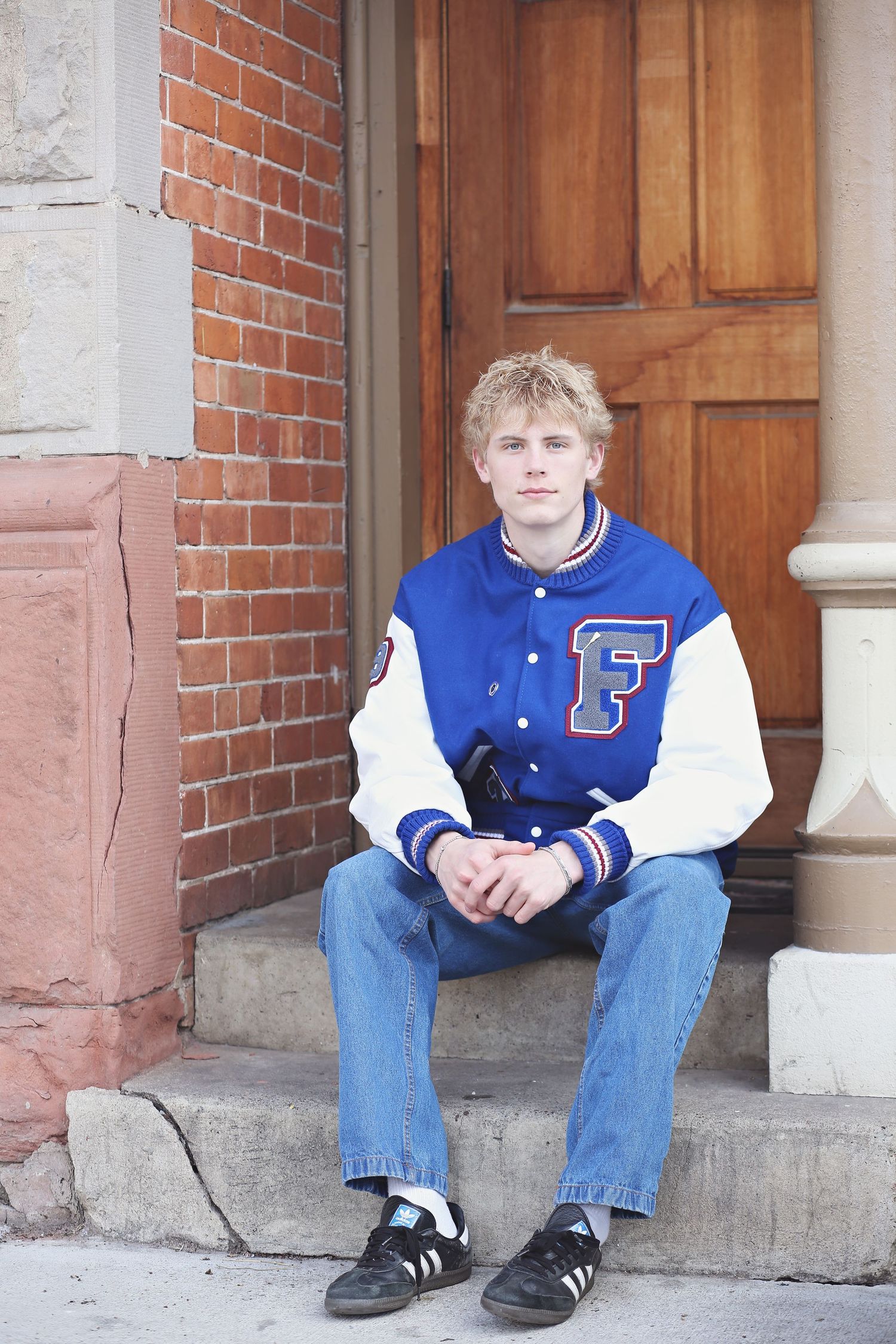 A person wearing a blue and white varsity letterman jacket sits on brick steps.