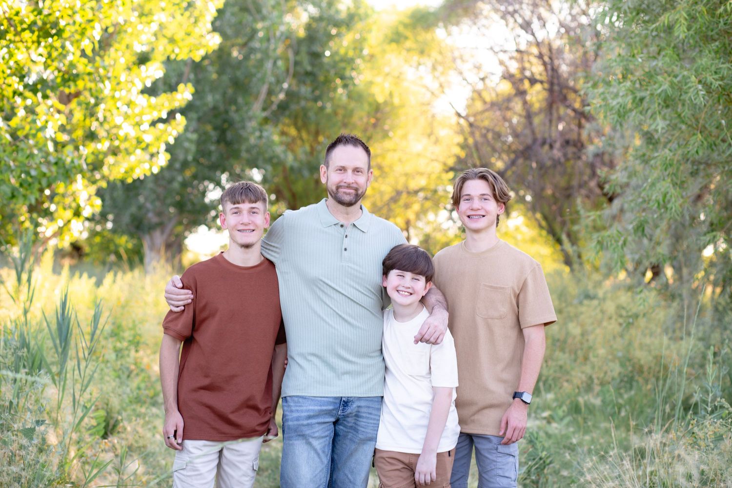A casual outdoor family portrait of four people with golden sunlight filtering through trees.