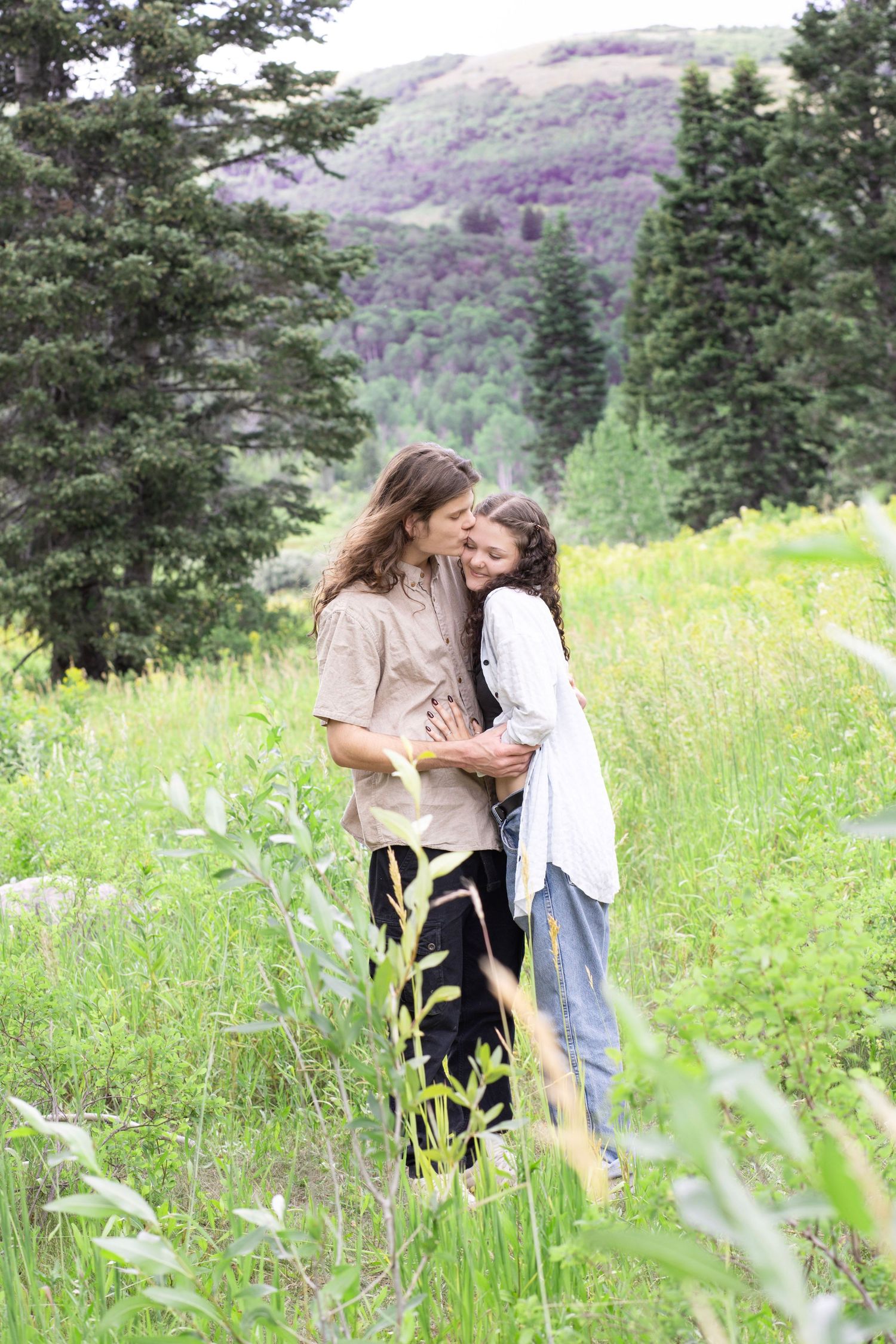 Romantic moment captured in mountain meadow with evergreen trees and natural lighting.