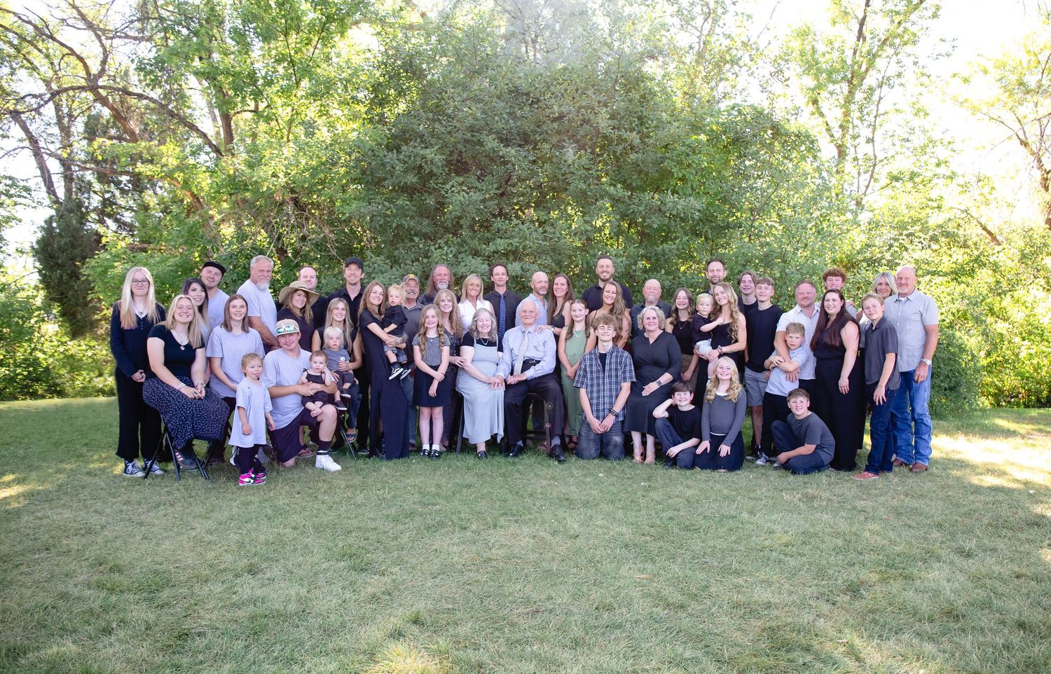 Extended family gathering photo with multiple generations posed on grassy hillside.