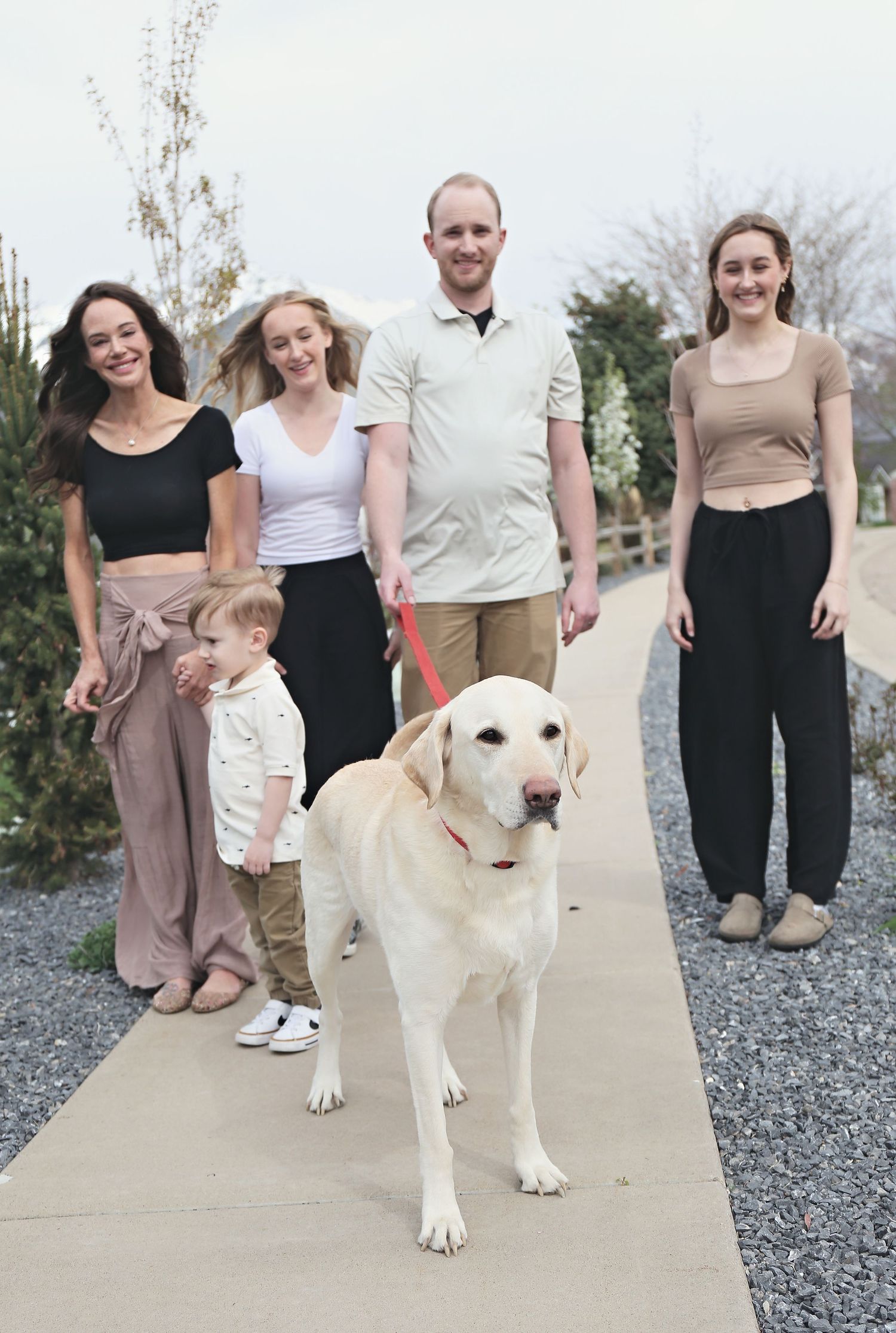A cream-colored dog walks with a group on a gravel path outdoors.